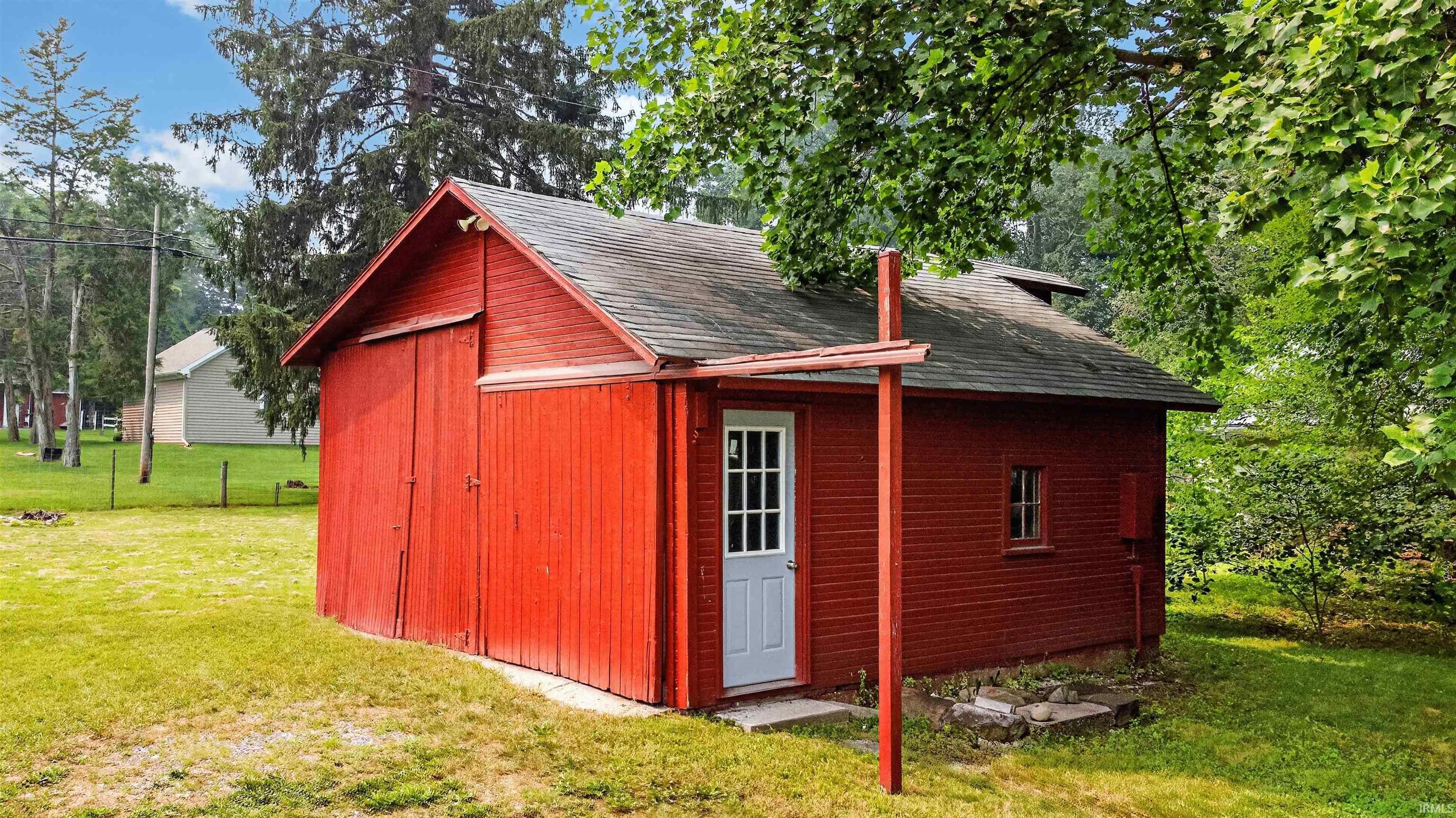 Red outbuilding with horizontal siding, a gabled roof, and a single white entry door with glass panes