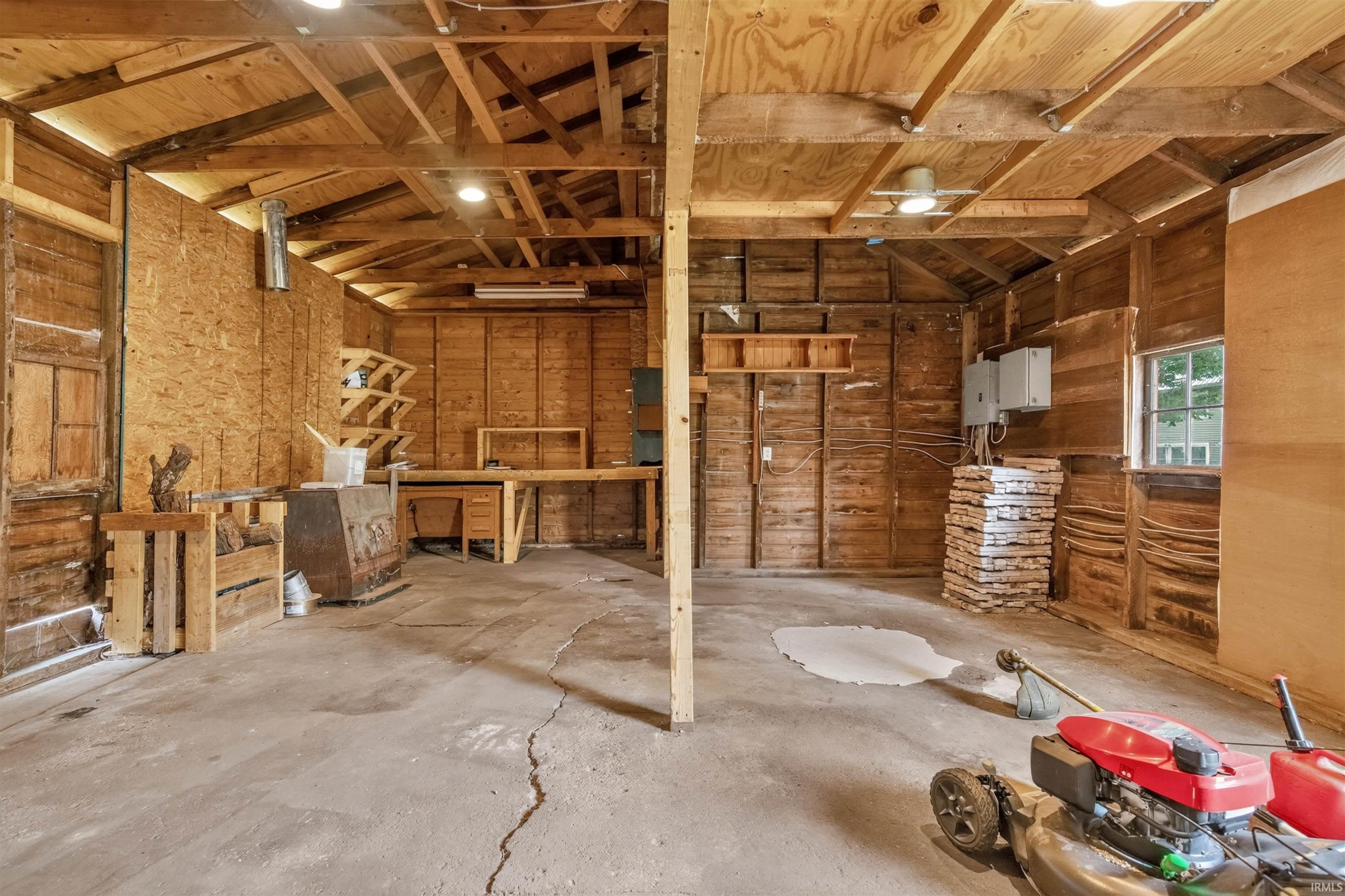 Spacious utility building featuring exposed wood framing, concrete flooring, built-in shelving, and a window for natural light