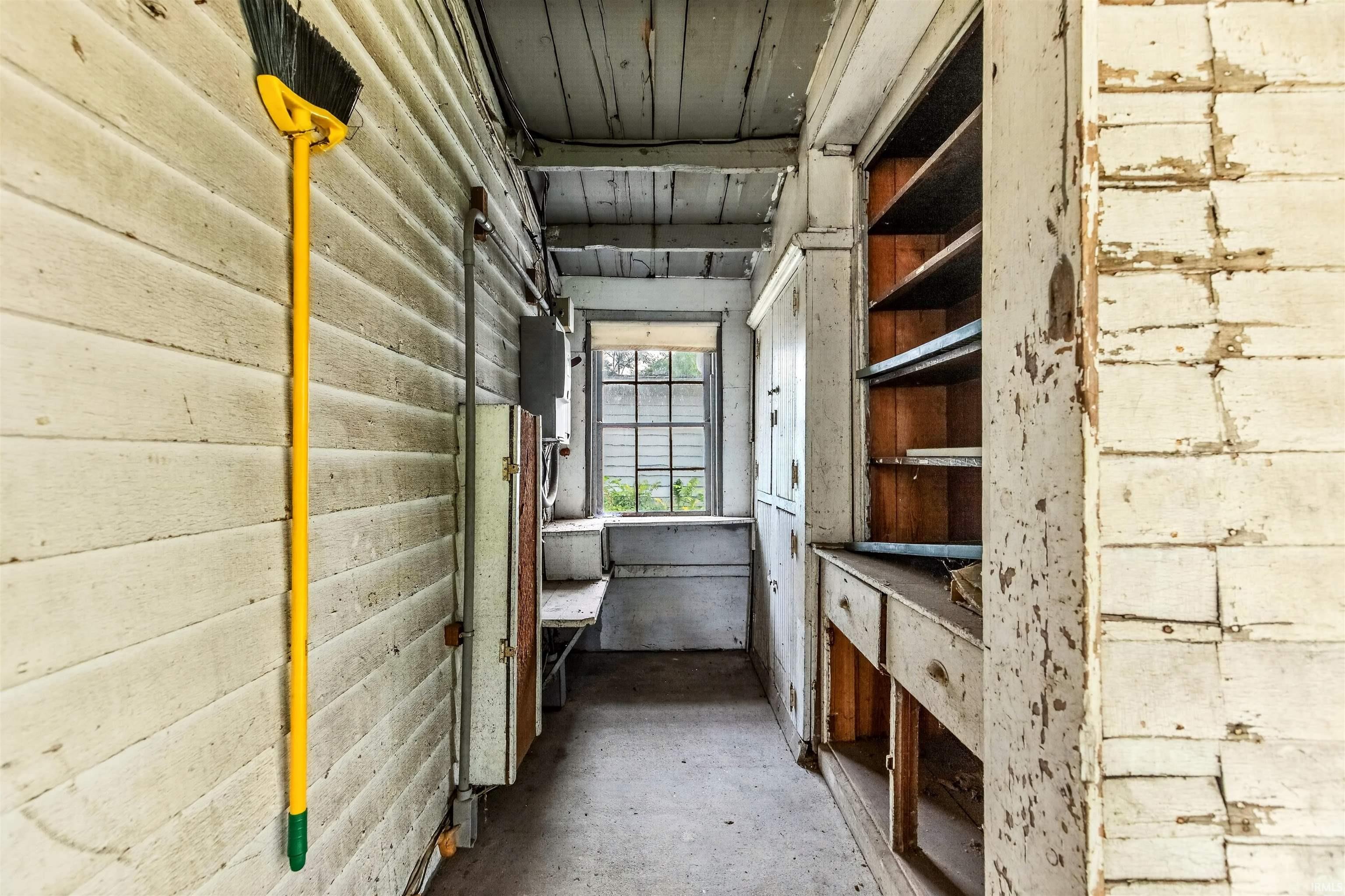 Enclosed utility space featuring built-in cabinetry, a window, and exposed wooden wall paneling