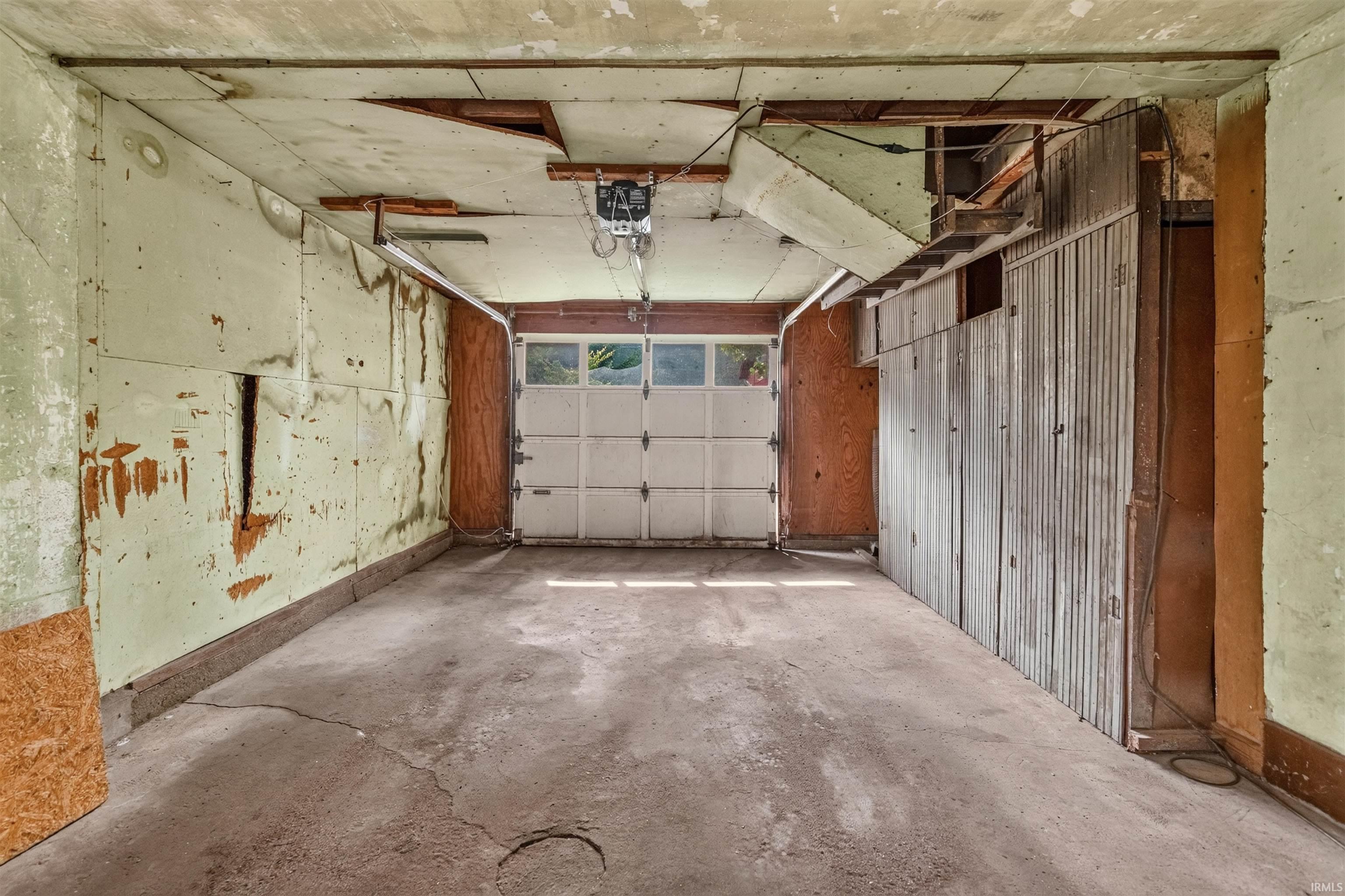 Garage interior featuring a white overhead door with upper window panels, exposed wood paneling, corrugated metal wall accents, and concrete flooring