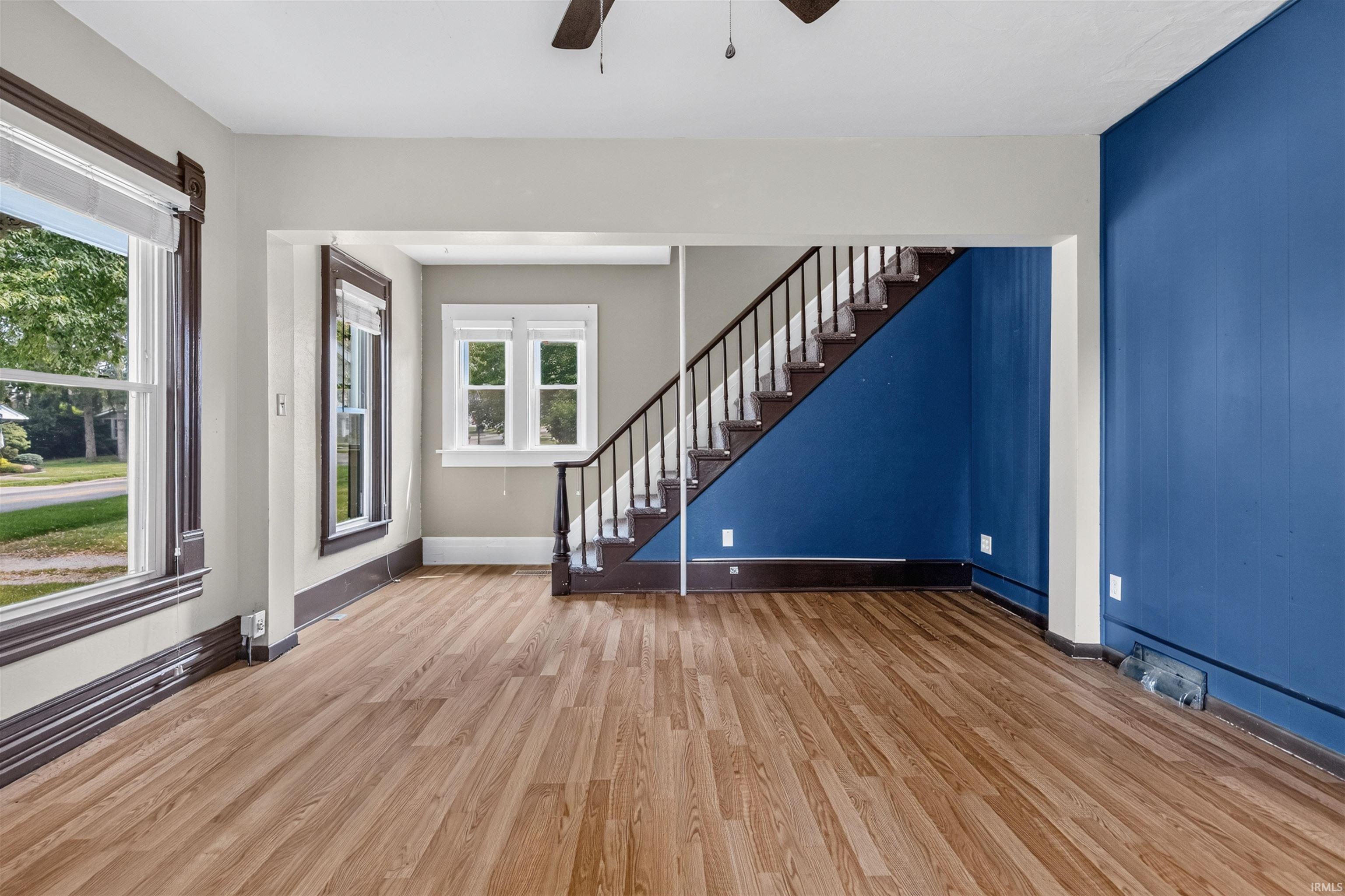 Spacious room featuring wood-finish flooring, a prominent staircase with dark wood railings, and a bold accent wall