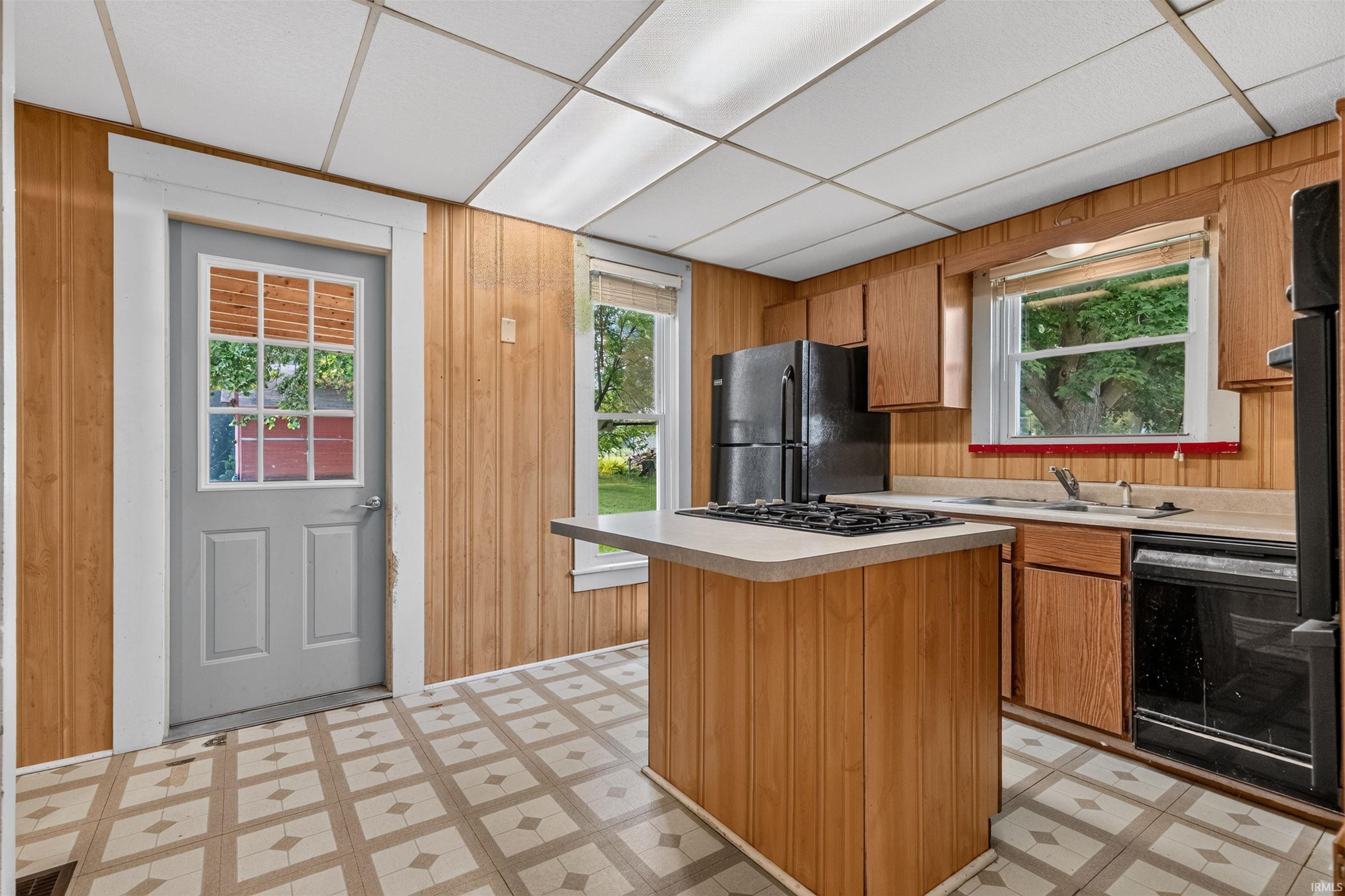 Kitchen featuring wood-panel walls, patterned flooring, and a central island with an integrated cooktop