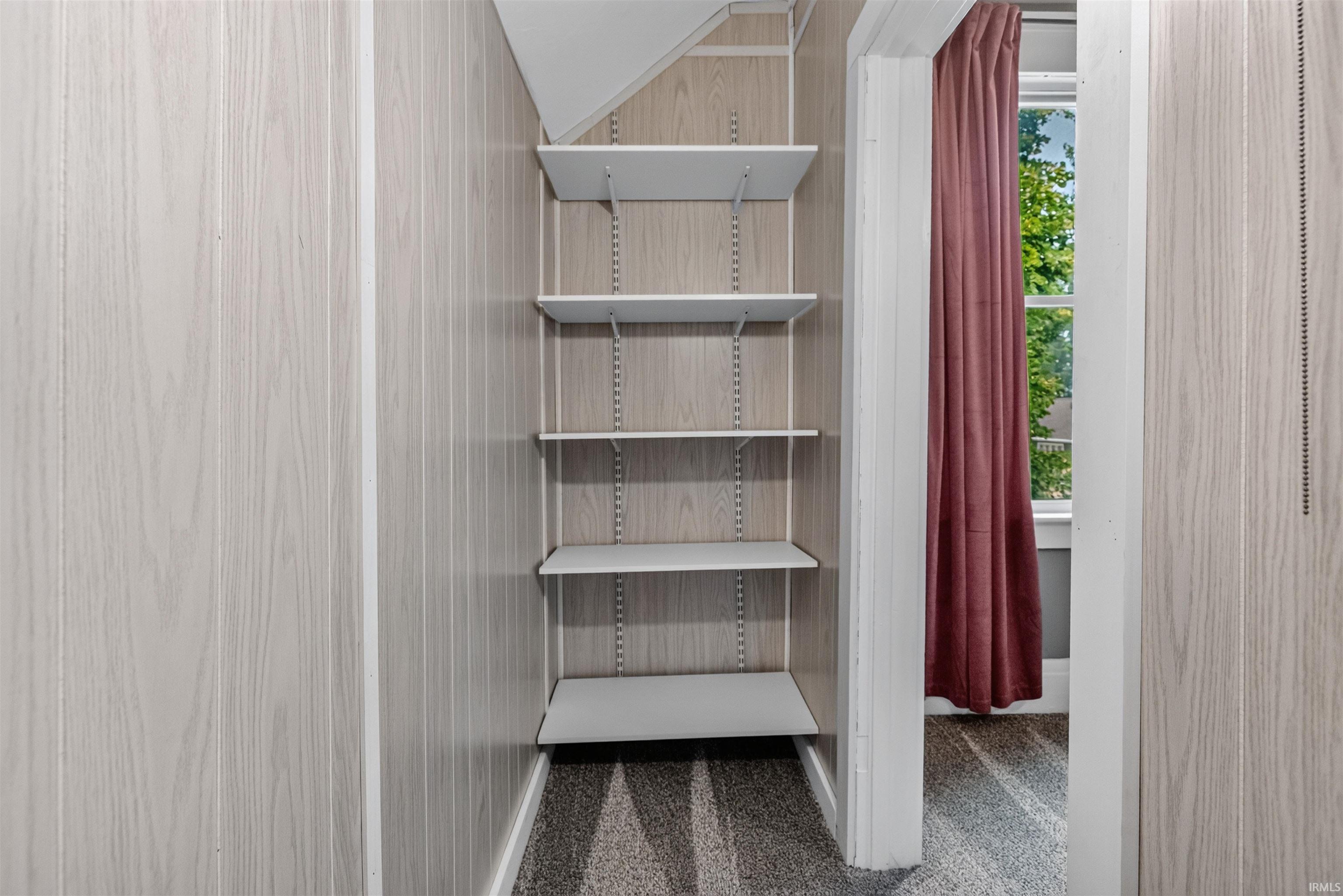 Built-in shelving system featuring adjustable white shelves, light wood-finish wall paneling, and gray textured carpeting