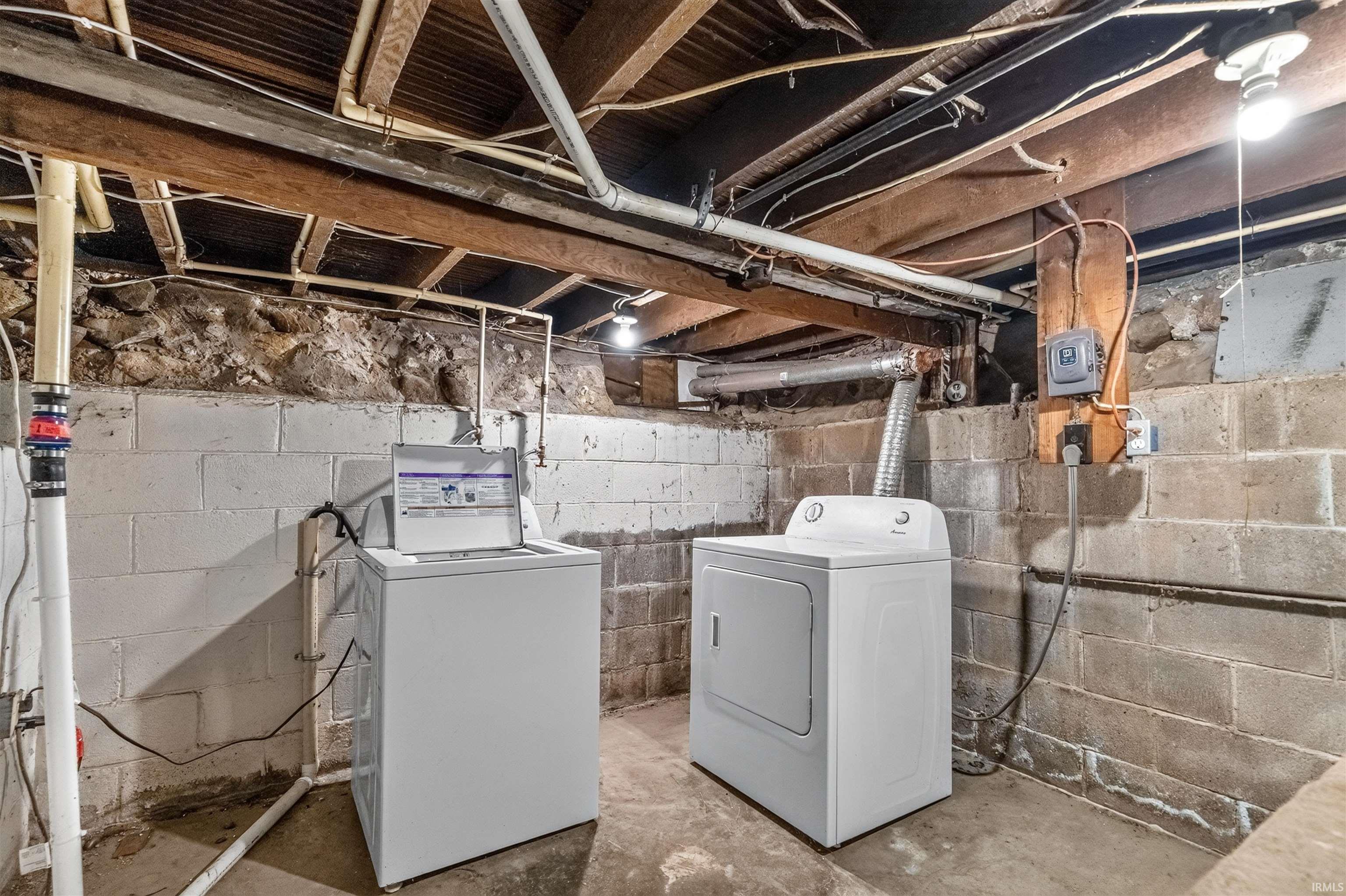 Laundry area in the basement with concrete block walls, exposed wood ceiling joists, and a concrete floor