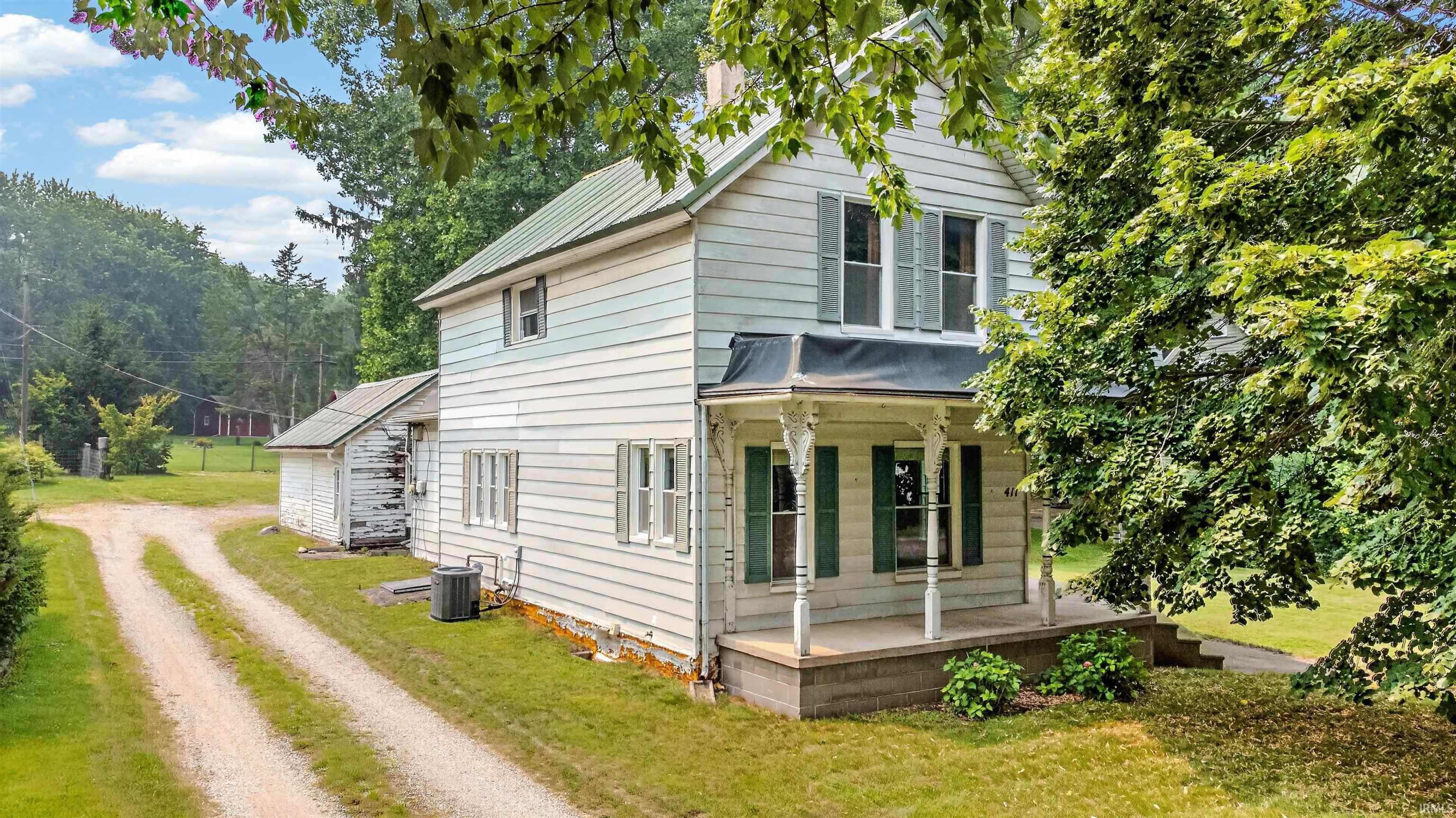 Two-story exterior featuring a front porch with decorative columns, green-painted shutters, and a metal roof