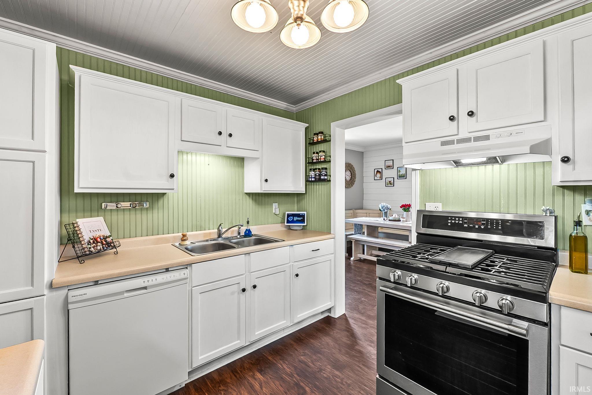 Kitchen featuring white cabinetry, a double basin stainless steel sink, a stainless steel range with a griddle, a white dishwasher, and wood-finish flooring