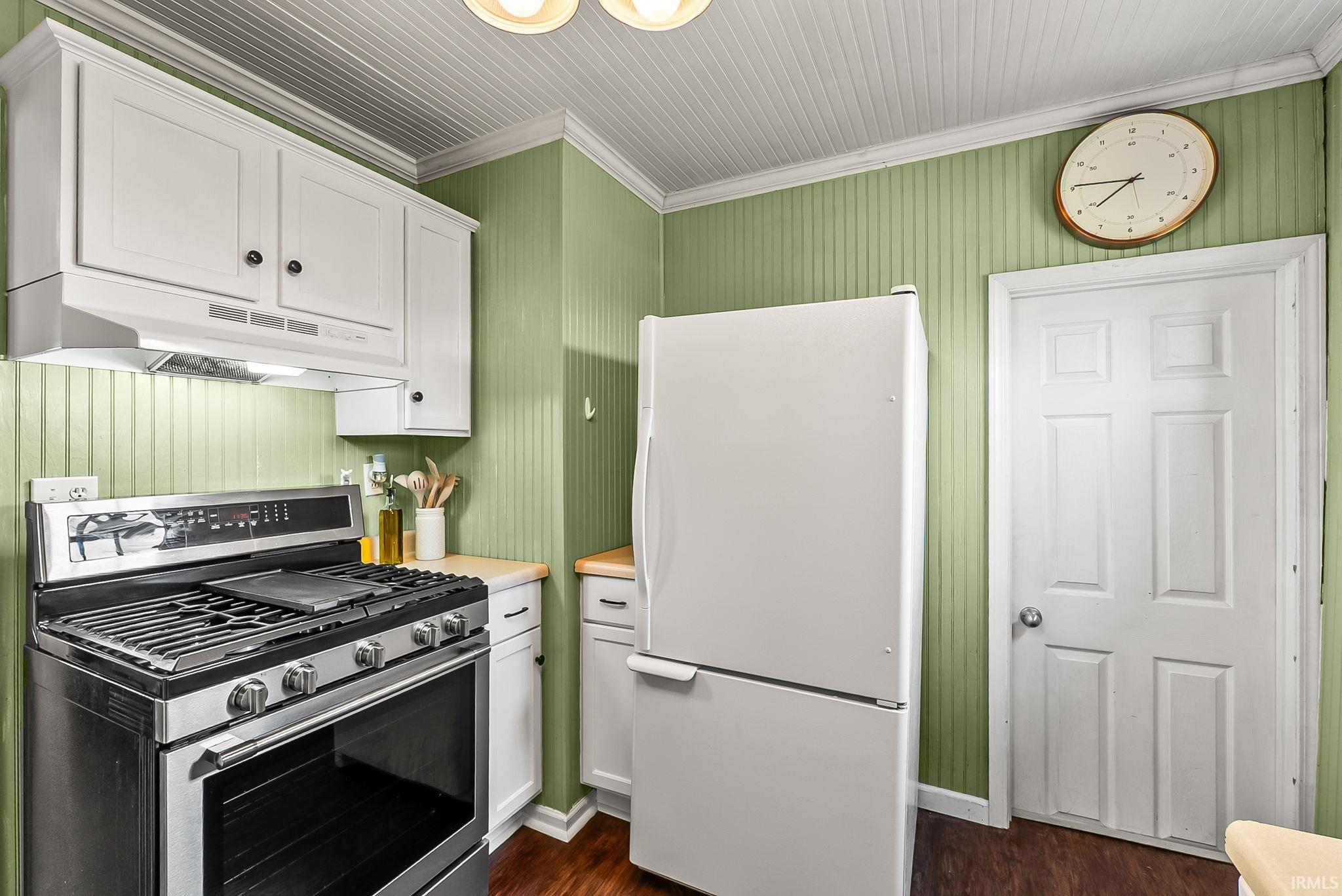 Kitchen featuring stainless steel range with overhead ventilation, white cabinetry with black hardware, wood-finish flooring, and a paneled ceiling