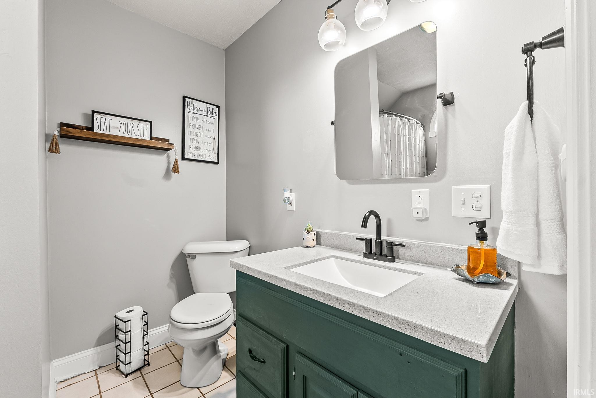 Bathroom featuring a dark green vanity with a white countertop and integrated sink, matte black faucet, and a rectangular mirror