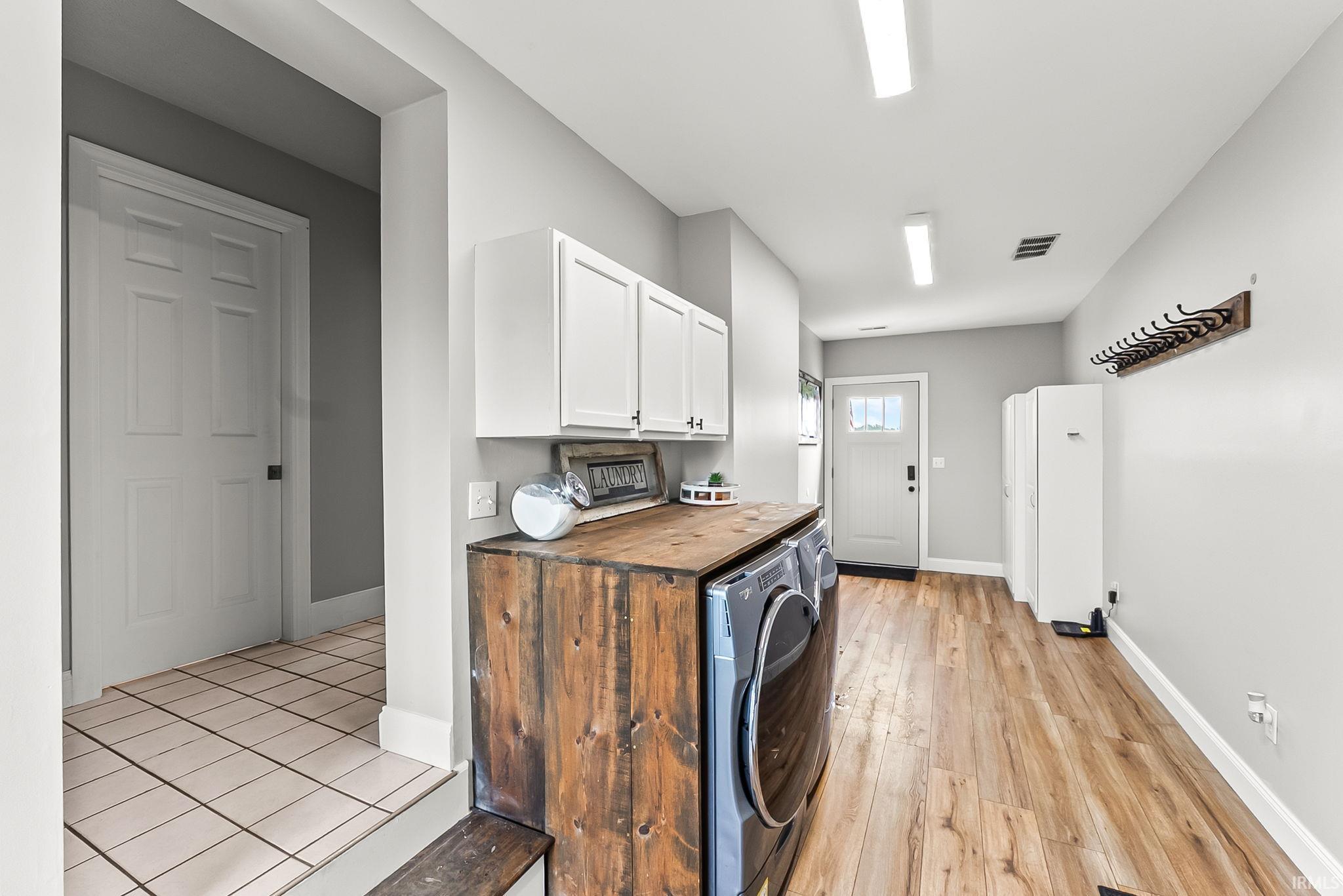 Laundry area featuring wood-finish flooring, white cabinetry, and a wood-tone counter