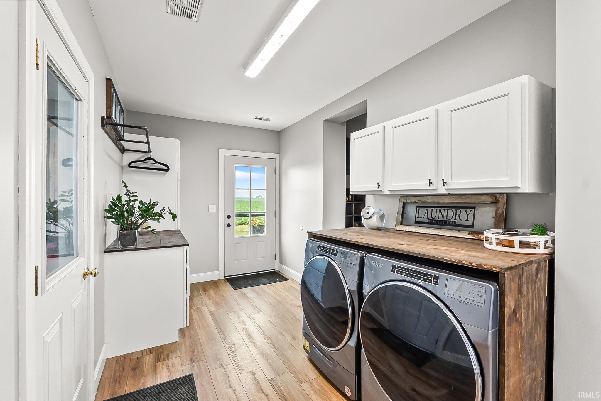 Laundry room featuring wood-finish flooring, white cabinetry, a built-in wood countertop, and a glass-paneled exterior door