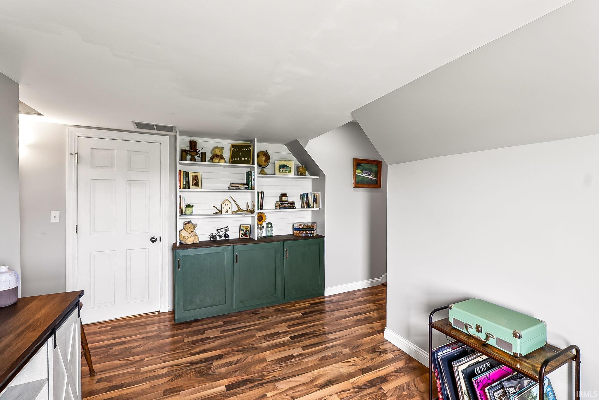 Attic space featuring wood-finish flooring, white built-in shelving, and a built-in green cabinet