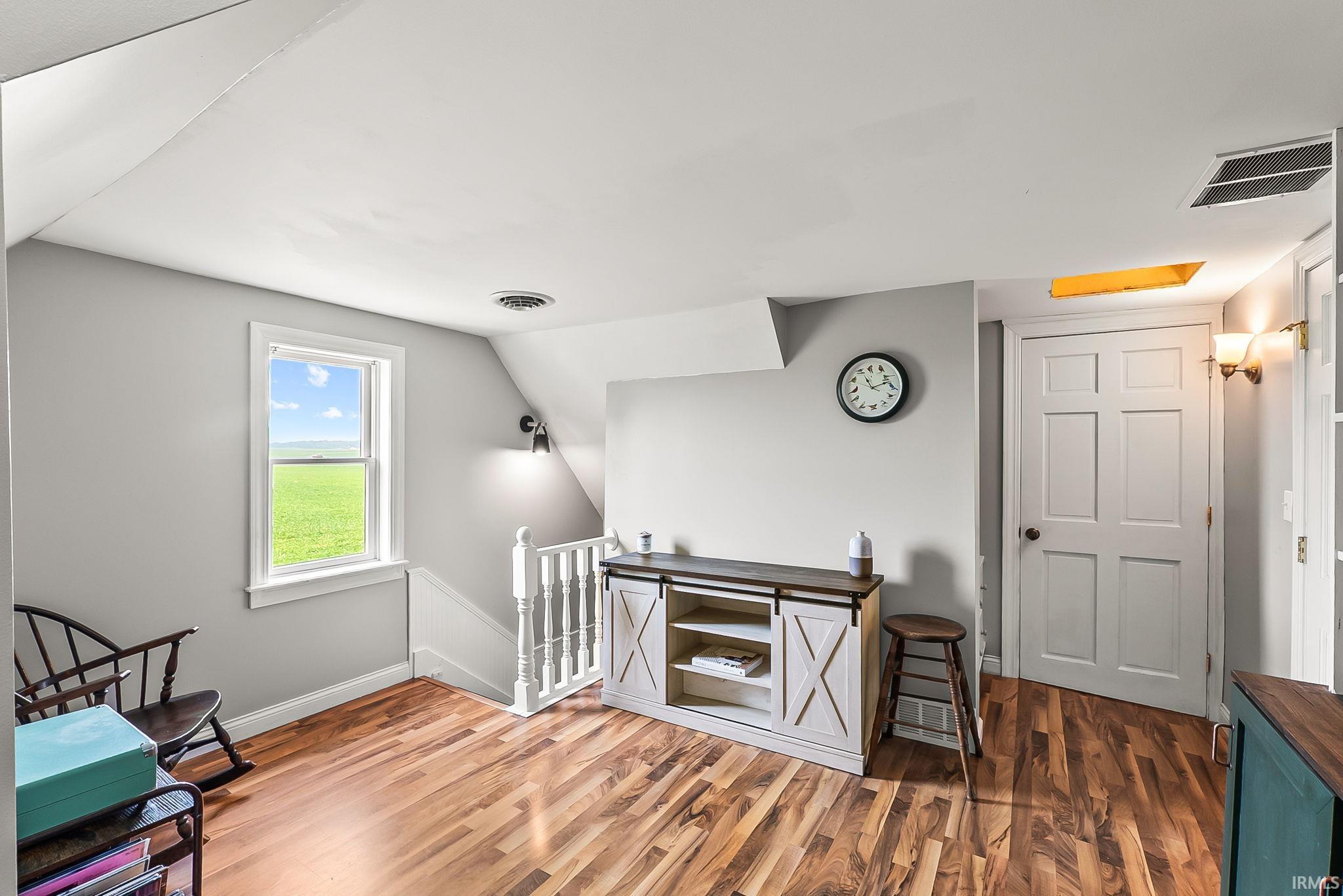 Wood-finish flooring anchors this bright space featuring a panel door, white window framing, and a white baluster railing