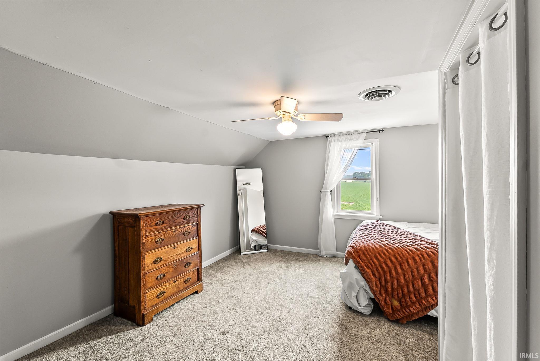 Carpeted room featuring a ceiling fan, sloped ceiling detail, and a window with a green outdoor expanse