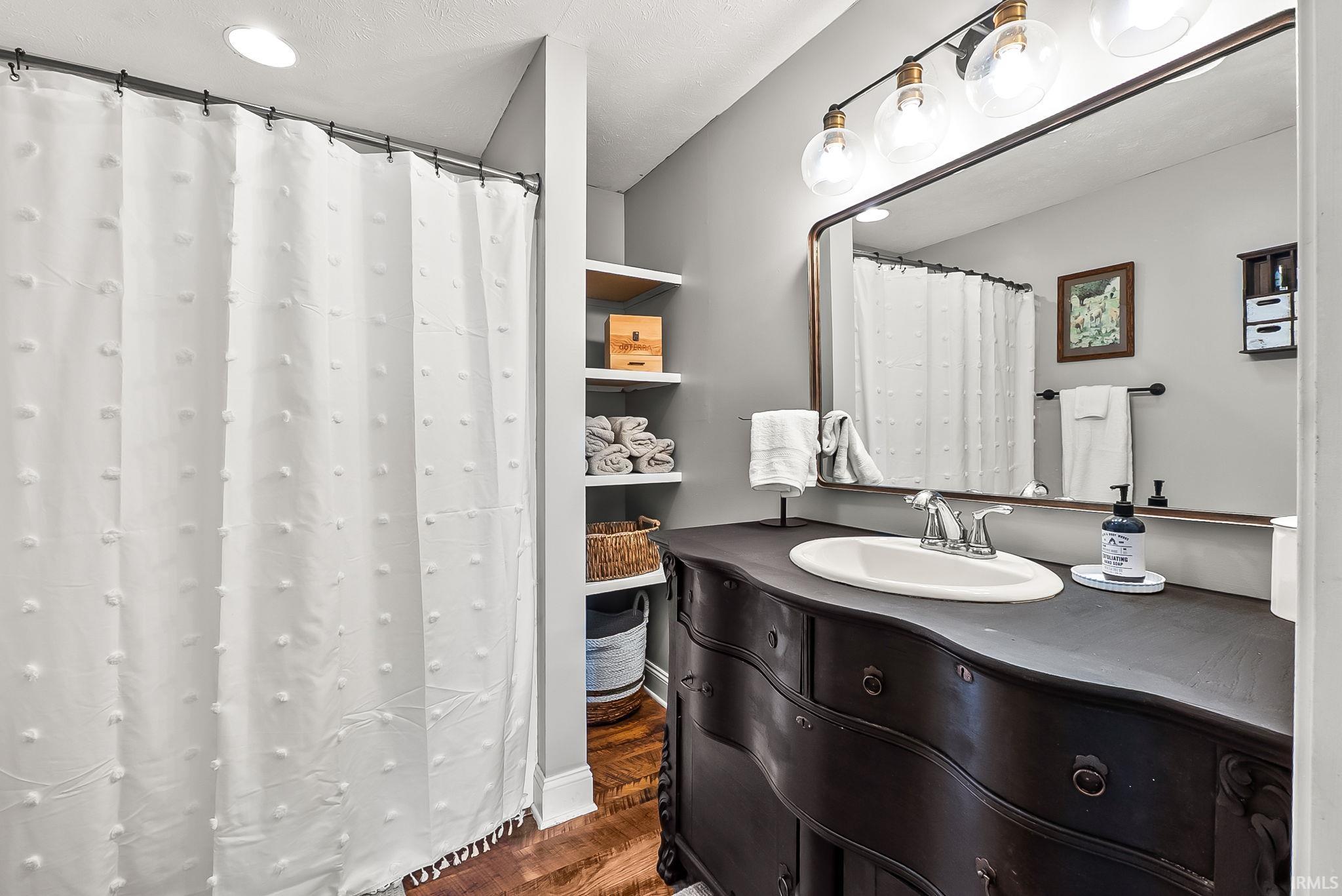 Bathroom vanity featuring an integrated oval sink, chrome faucet, and a large mirror with a four-bulb vanity light