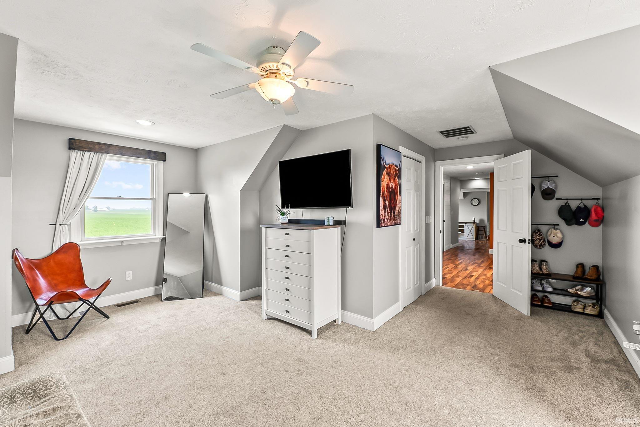 Carpeted room with a ceiling fan, window with wood-finish trim, and an angled ceiling