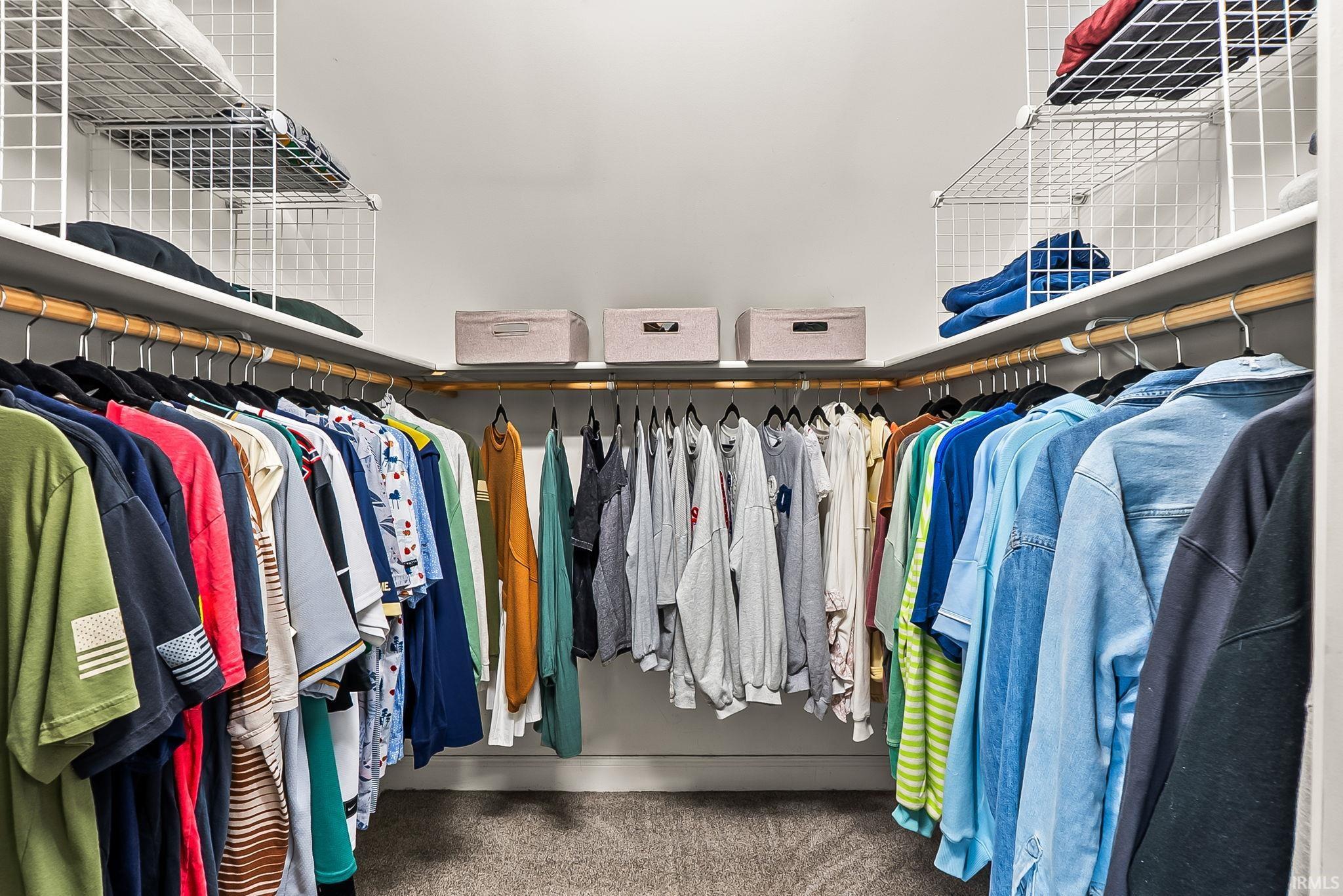 Expansive walk-in closet featuring floor-to-ceiling white shelving, multiple hanging rods, and an L-shaped configuration