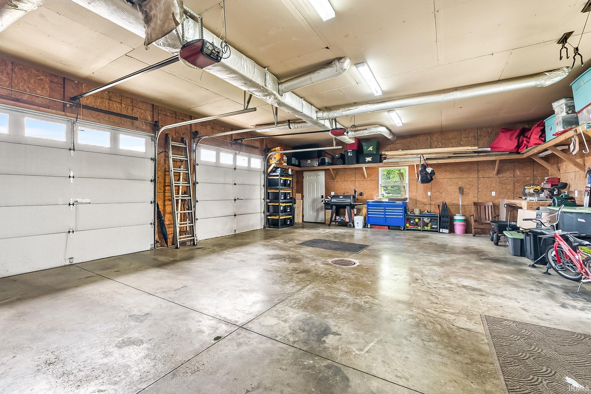 Spacious garage featuring two overhead doors with transom windows, exposed wood panel walls, and concrete flooring