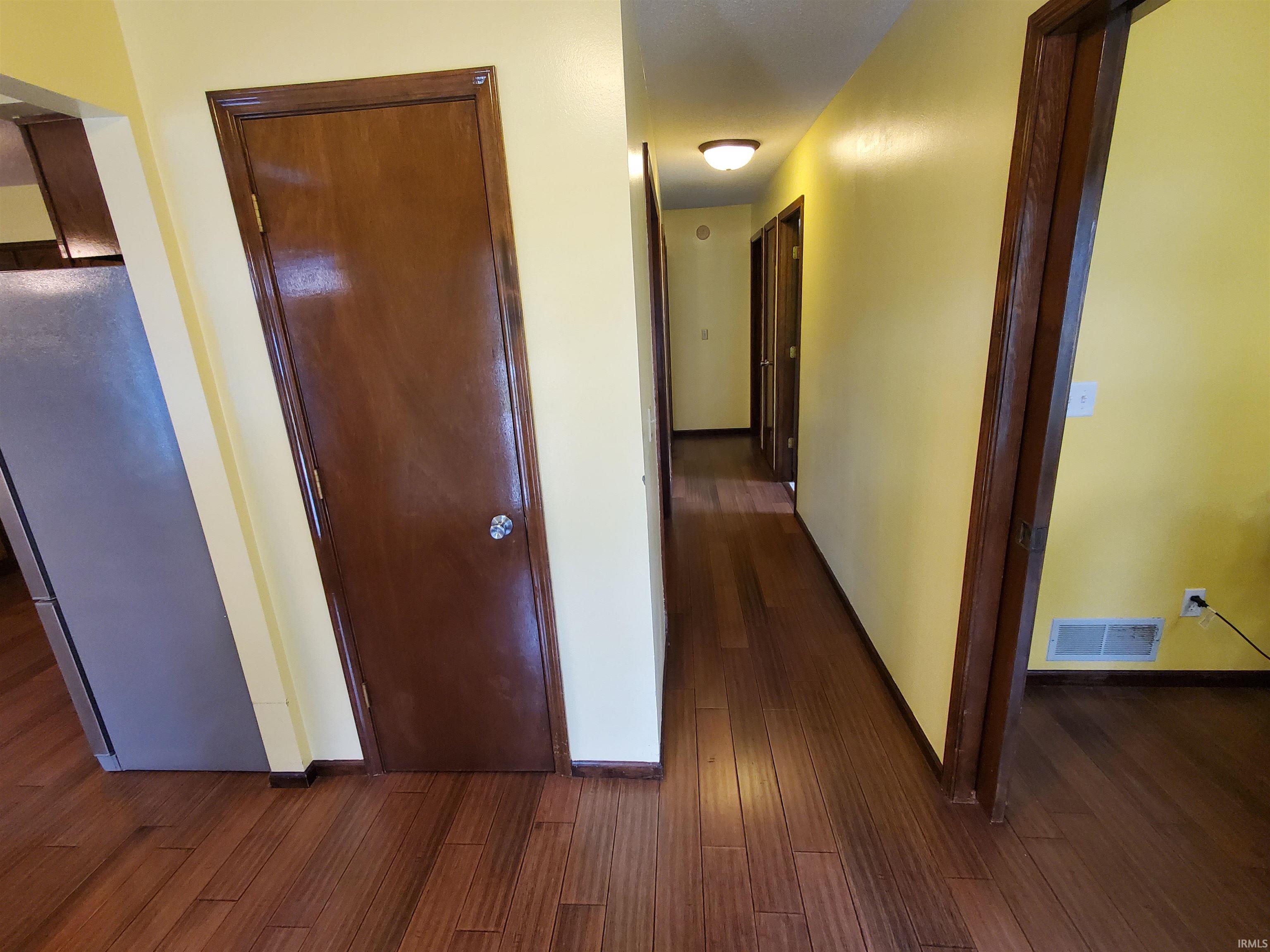 Hallway featuring wood-finish flooring, yellow walls, and multiple solid wood doors with dark trim