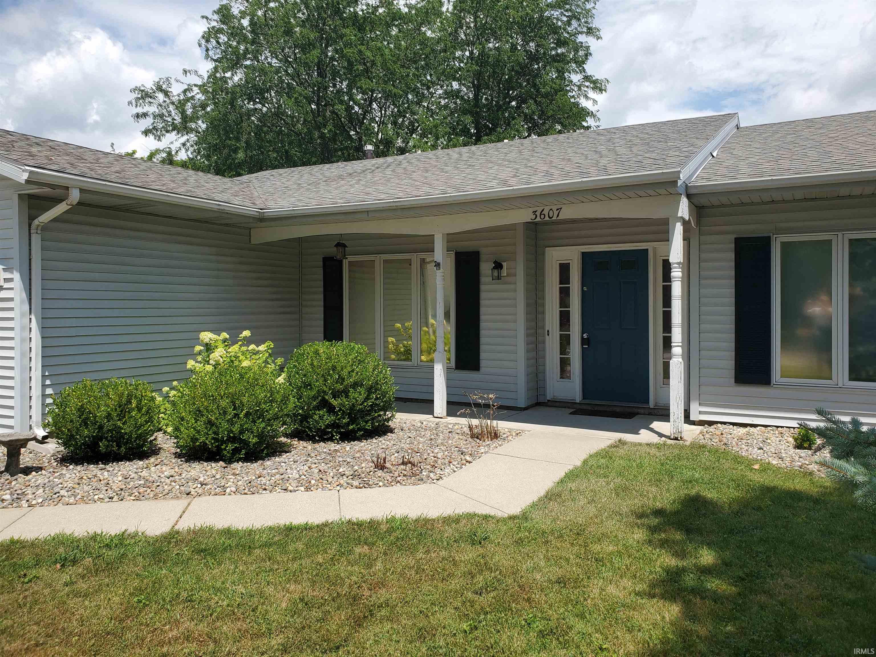 Ranch-style residence featuring light-colored siding, a covered entry, and a dark blue front door with sidelights