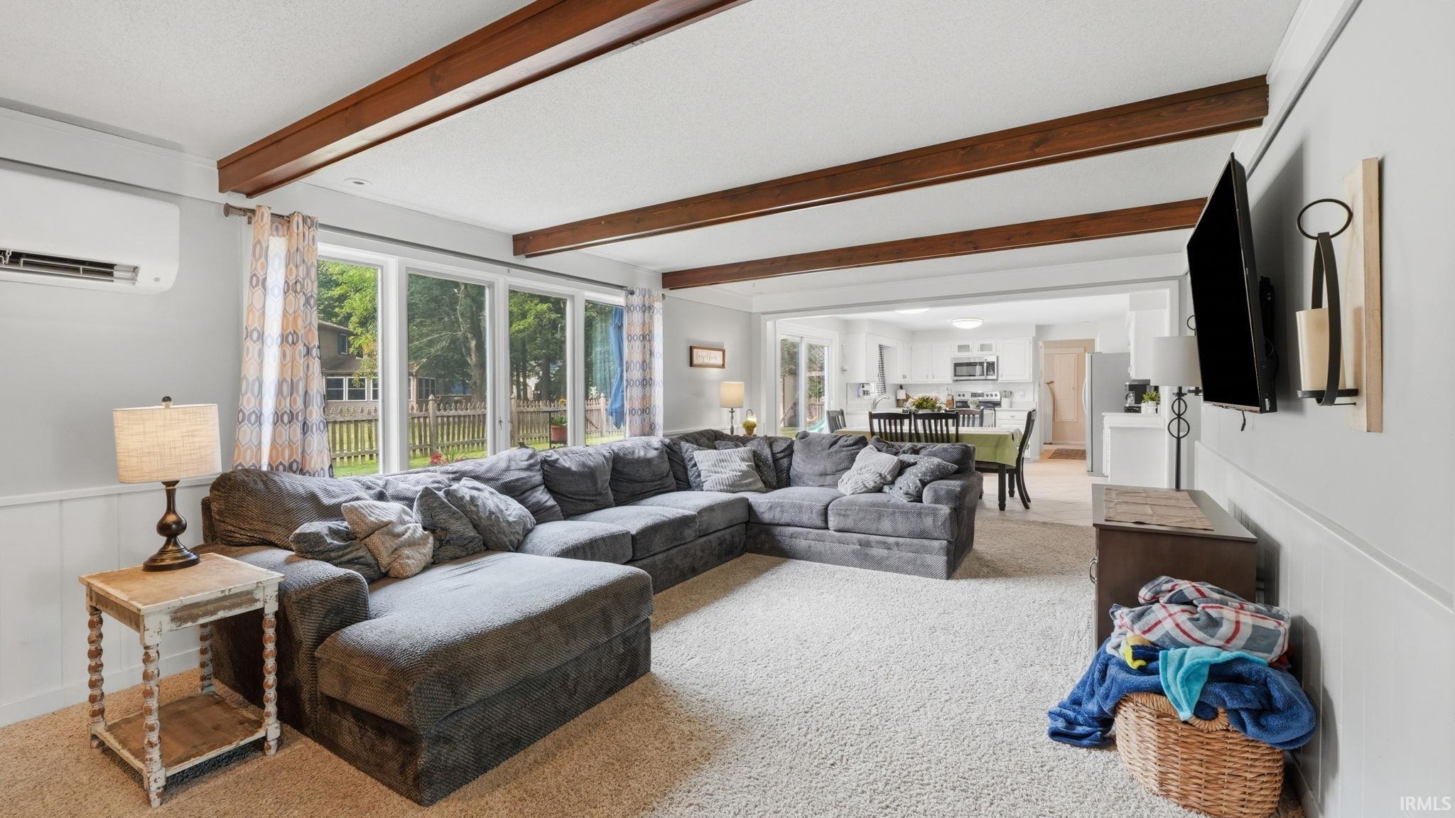 Living area featuring exposed wood-finish ceiling beams, an integrated air conditioning unit, and a wall of windows