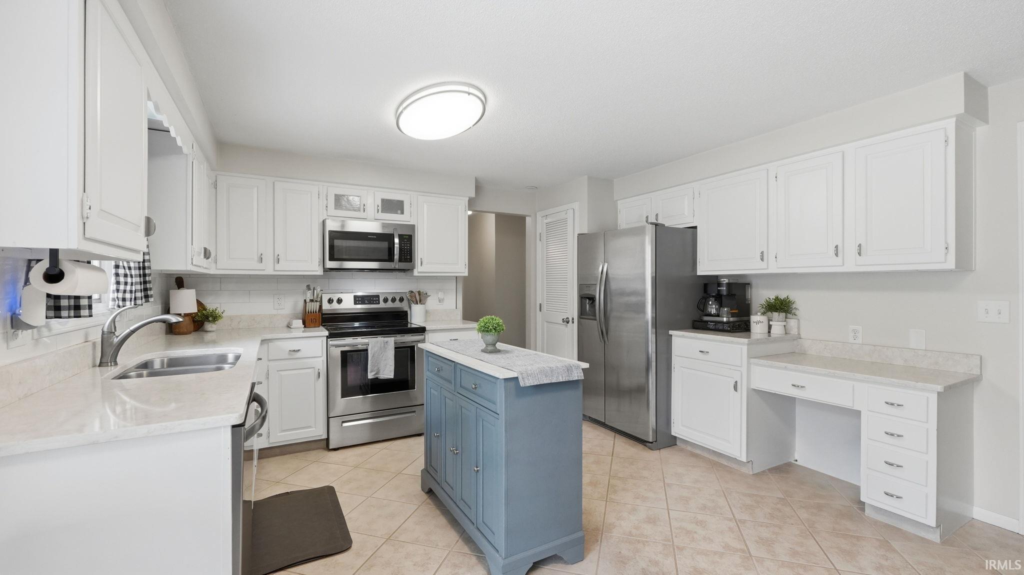 Bright kitchen featuring white cabinetry, light countertops, stainless steel appliances, a center island with storage, and tiled flooring