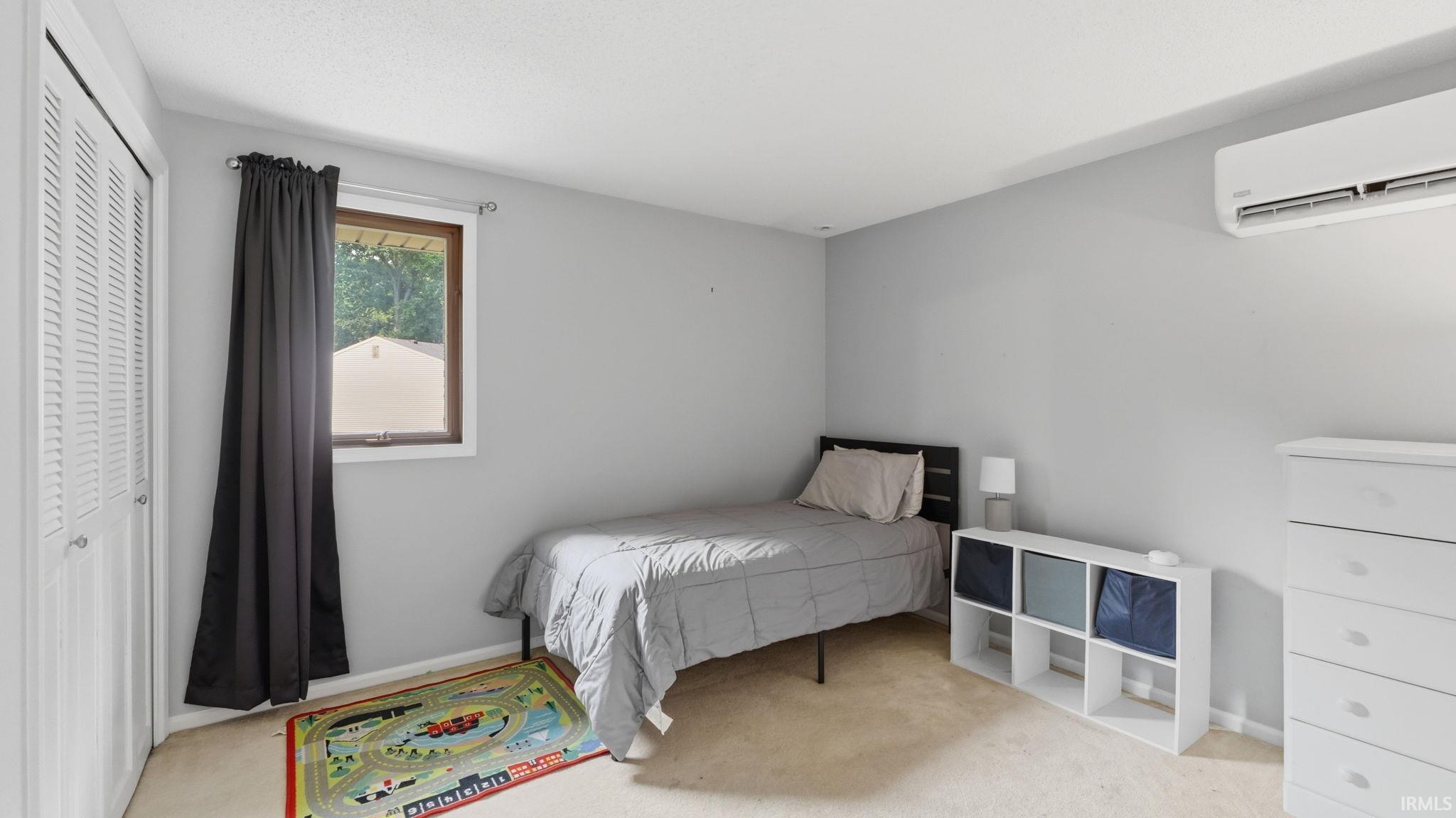 Bedroom featuring light gray walls, carpet flooring, a window with wood trim, and a white louvered closet door