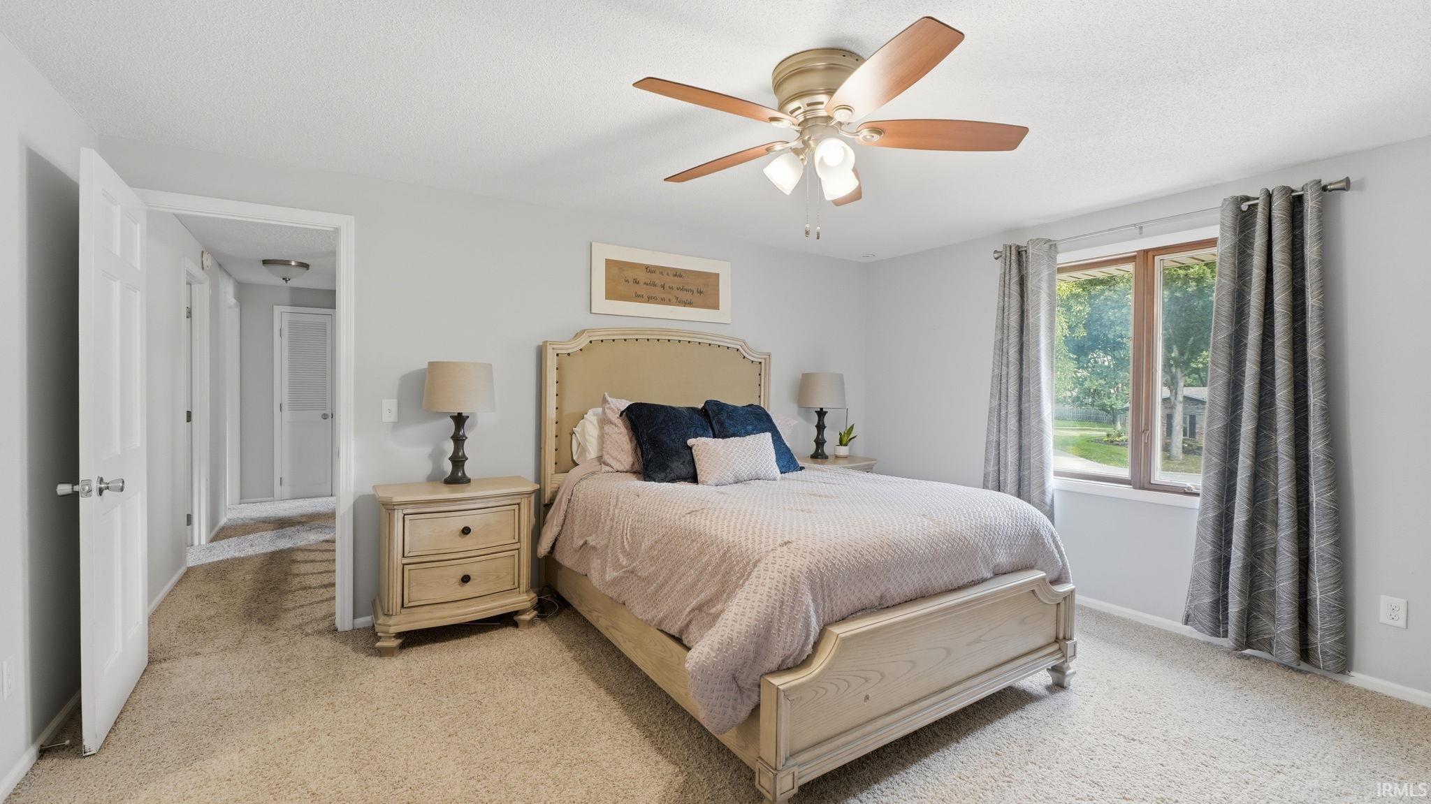 Bedroom featuring light gray wall paint, brown-framed window, ceiling fan with light kit, and carpet flooring