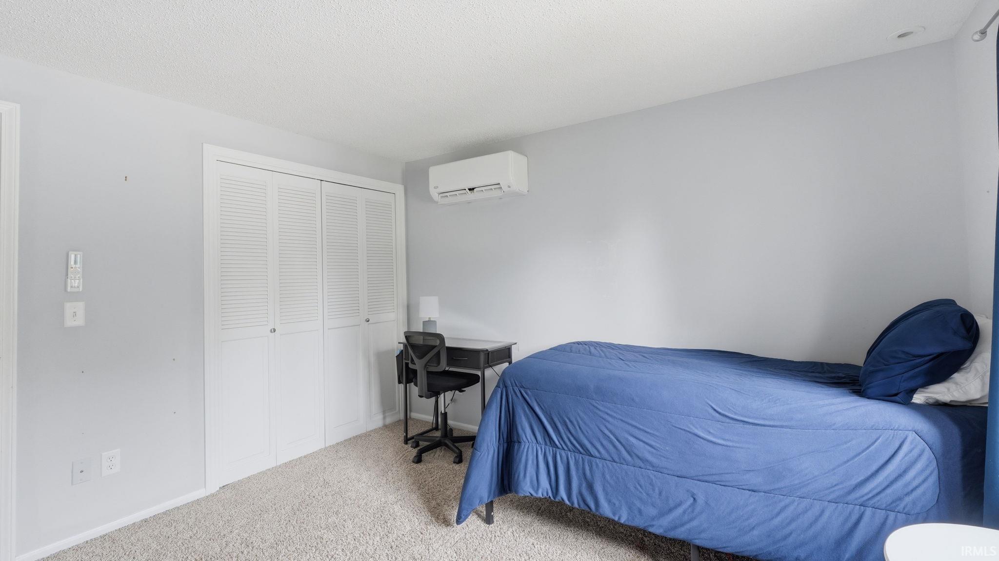 Carpeted bedroom with a mini-split system, louvered bi-fold closet doors, and light gray walls