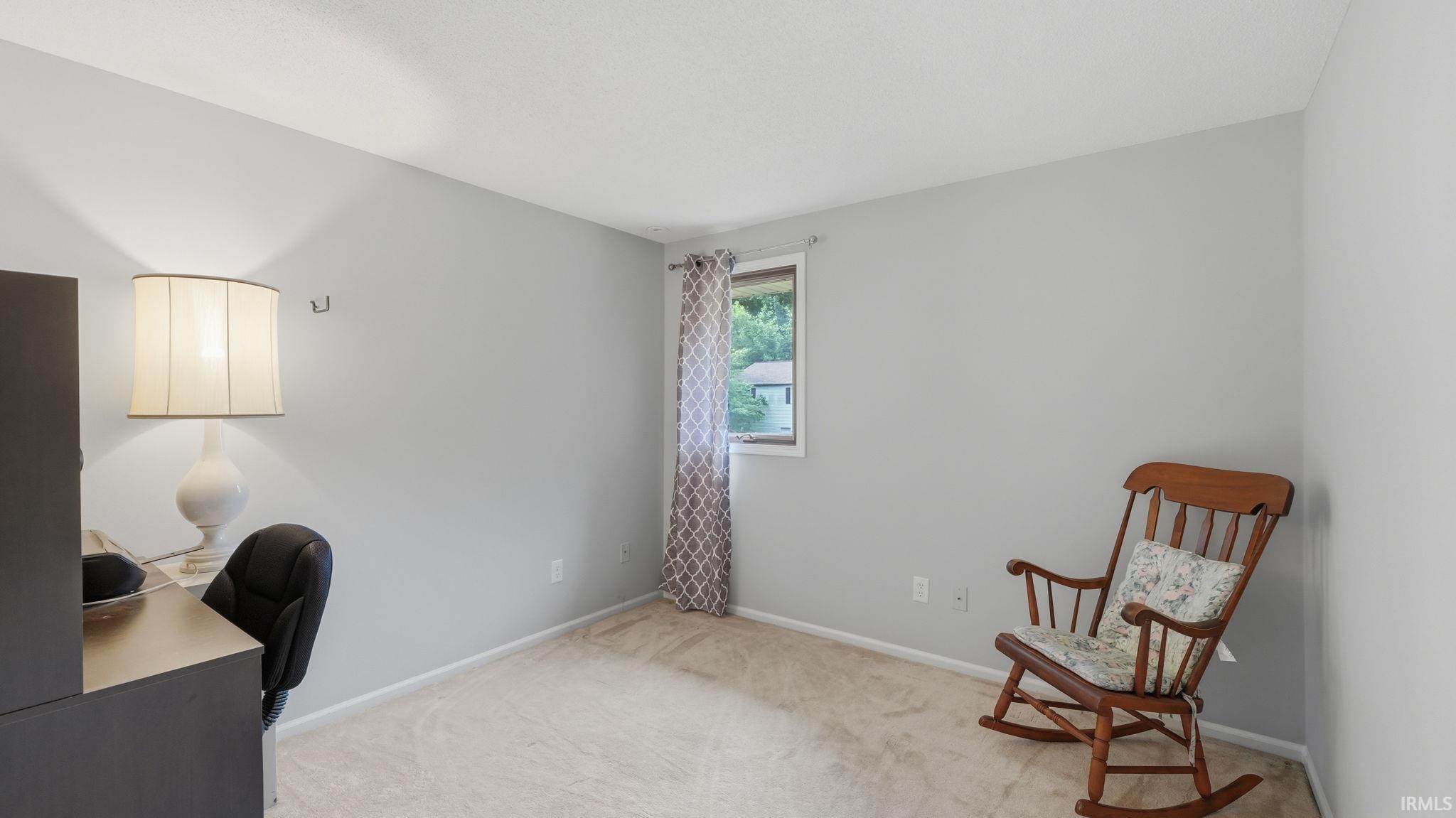 Light gray painted walls with neutral carpet flooring and a single window featuring patterned drapes