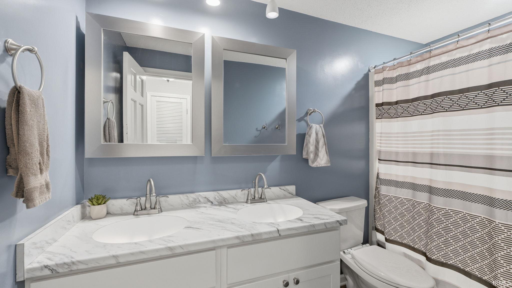 Bathroom featuring a dual vanity with a white marble-finish countertop, two undermount sinks, and brushed nickel faucets