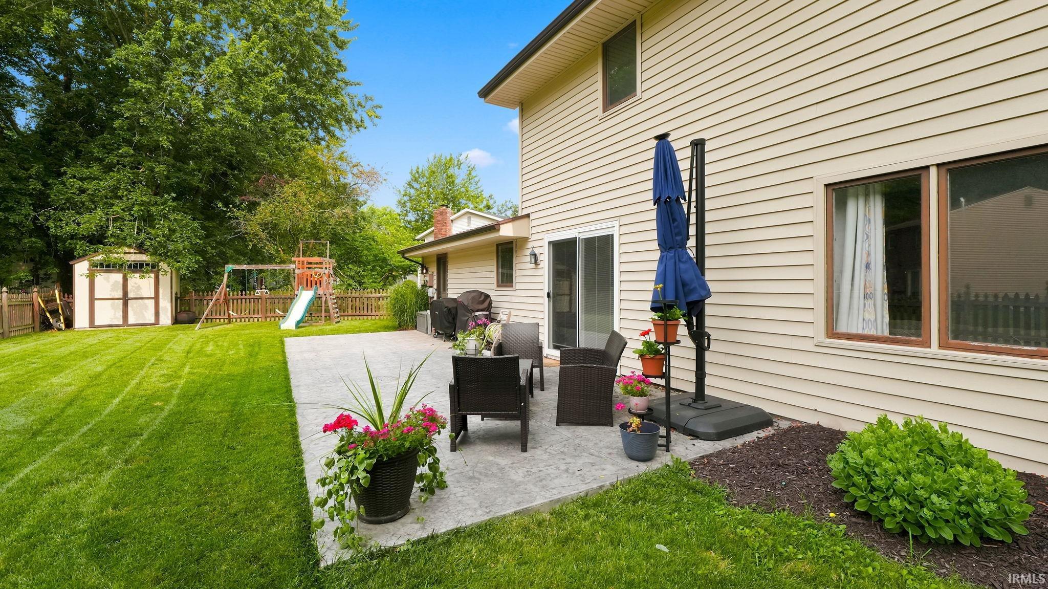 Expansive backyard featuring a concrete patio, a manicured lawn, and a wood storage shed