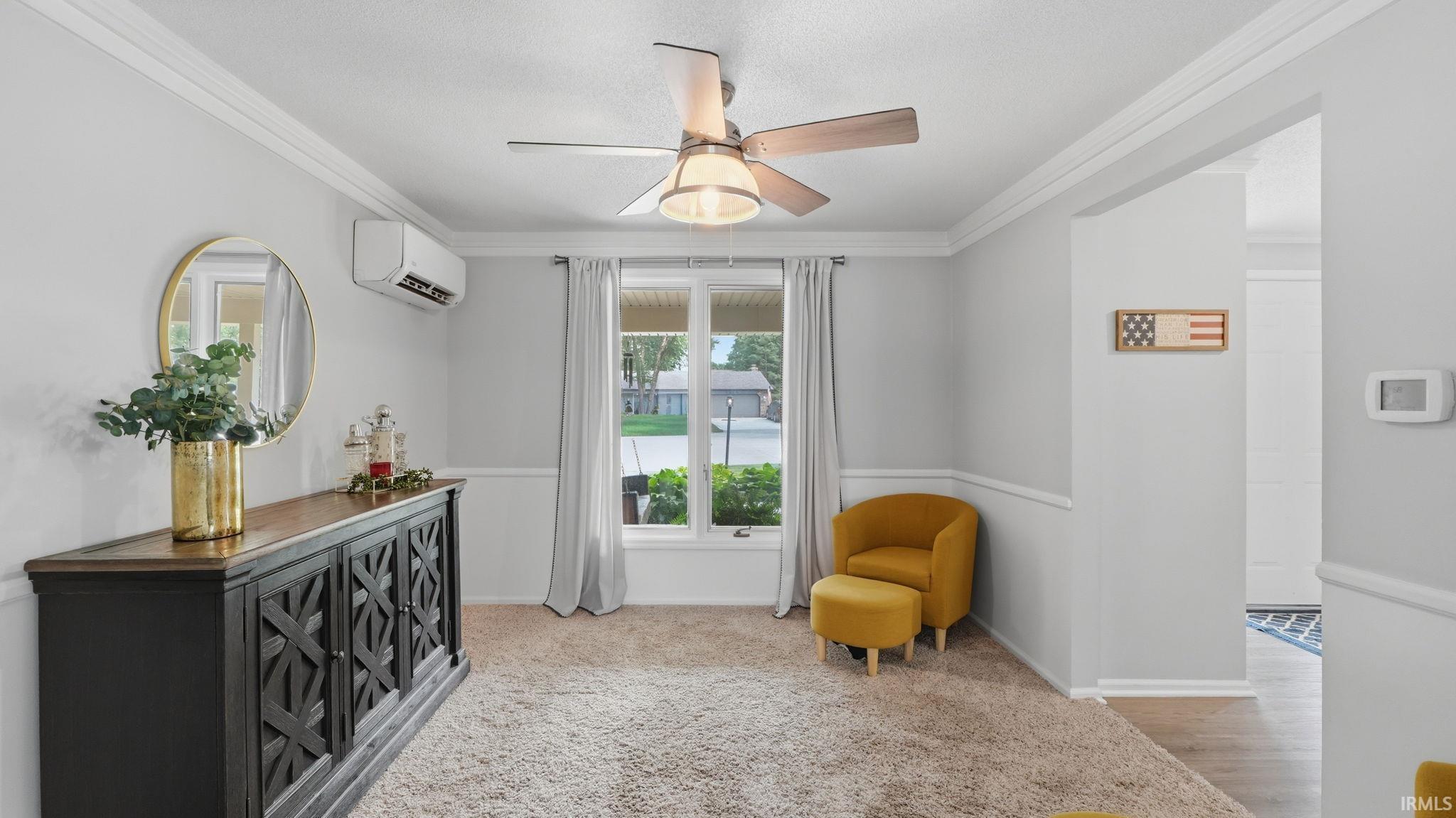 Interior room featuring a ceiling fan, a window with natural light, wall-mounted air conditioning unit, light-colored carpeting, and crown molding