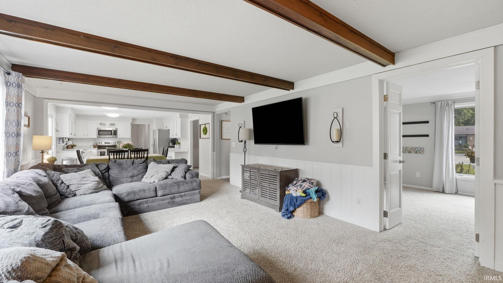 Living area featuring wood-finish ceiling beams and light-toned carpet