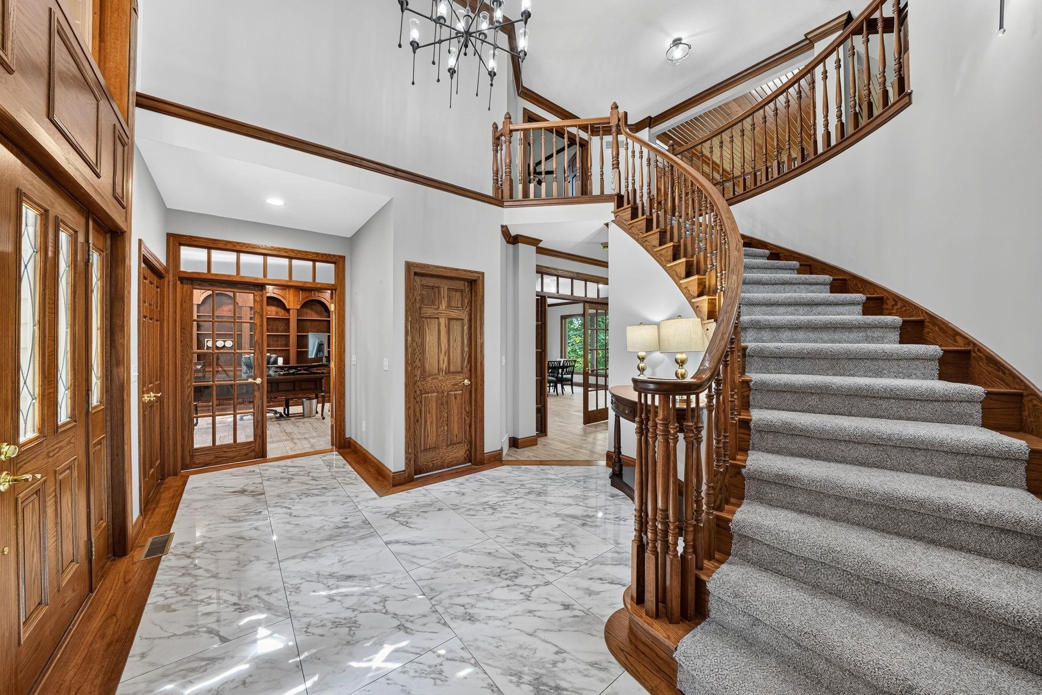 Grand foyer featuring a curved staircase with wood banister and carpeted treads, marble-look tile flooring, and double-height walls