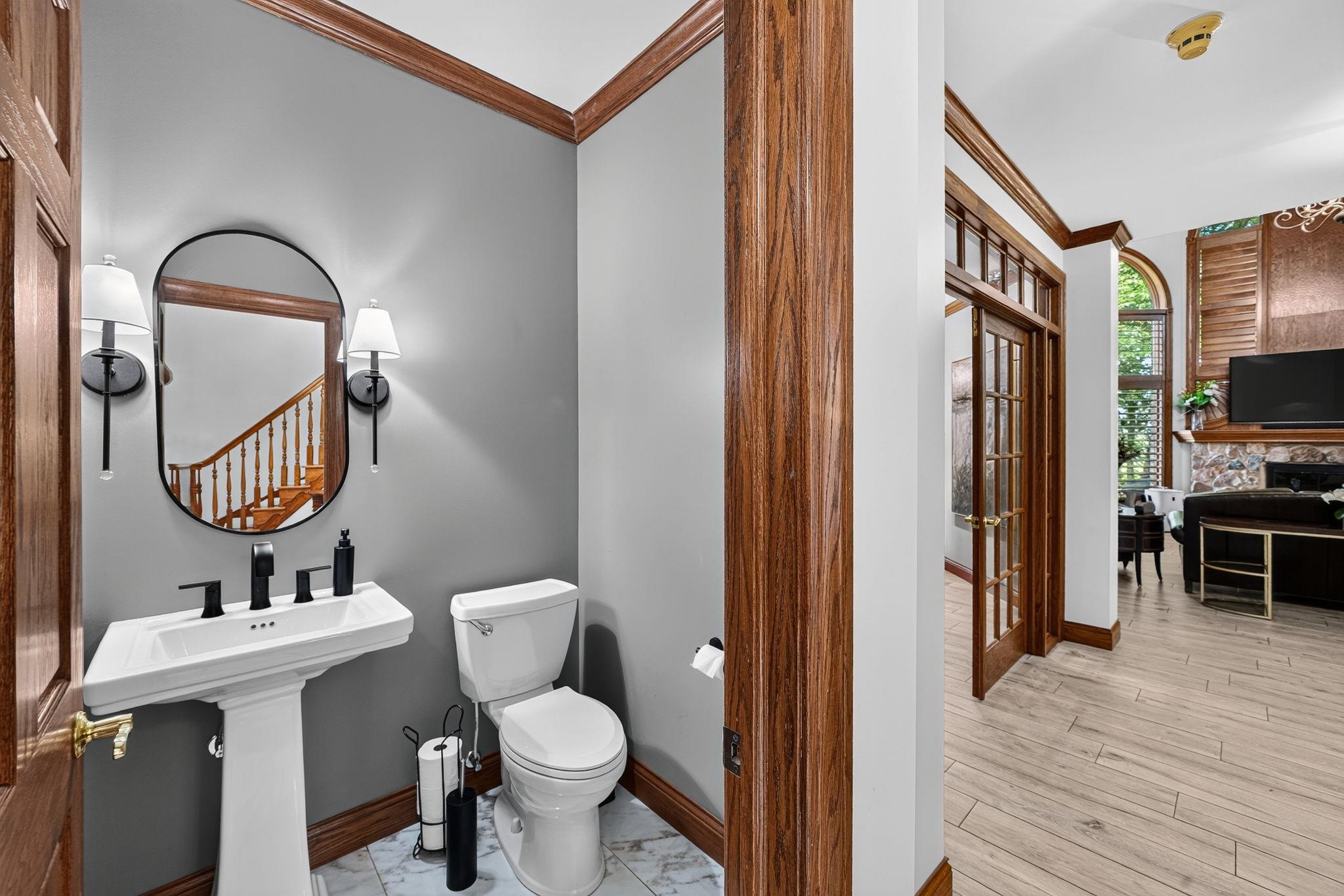 Pedestal sink with matte black faucet, oval mirror, and wall sconces against gray walls
