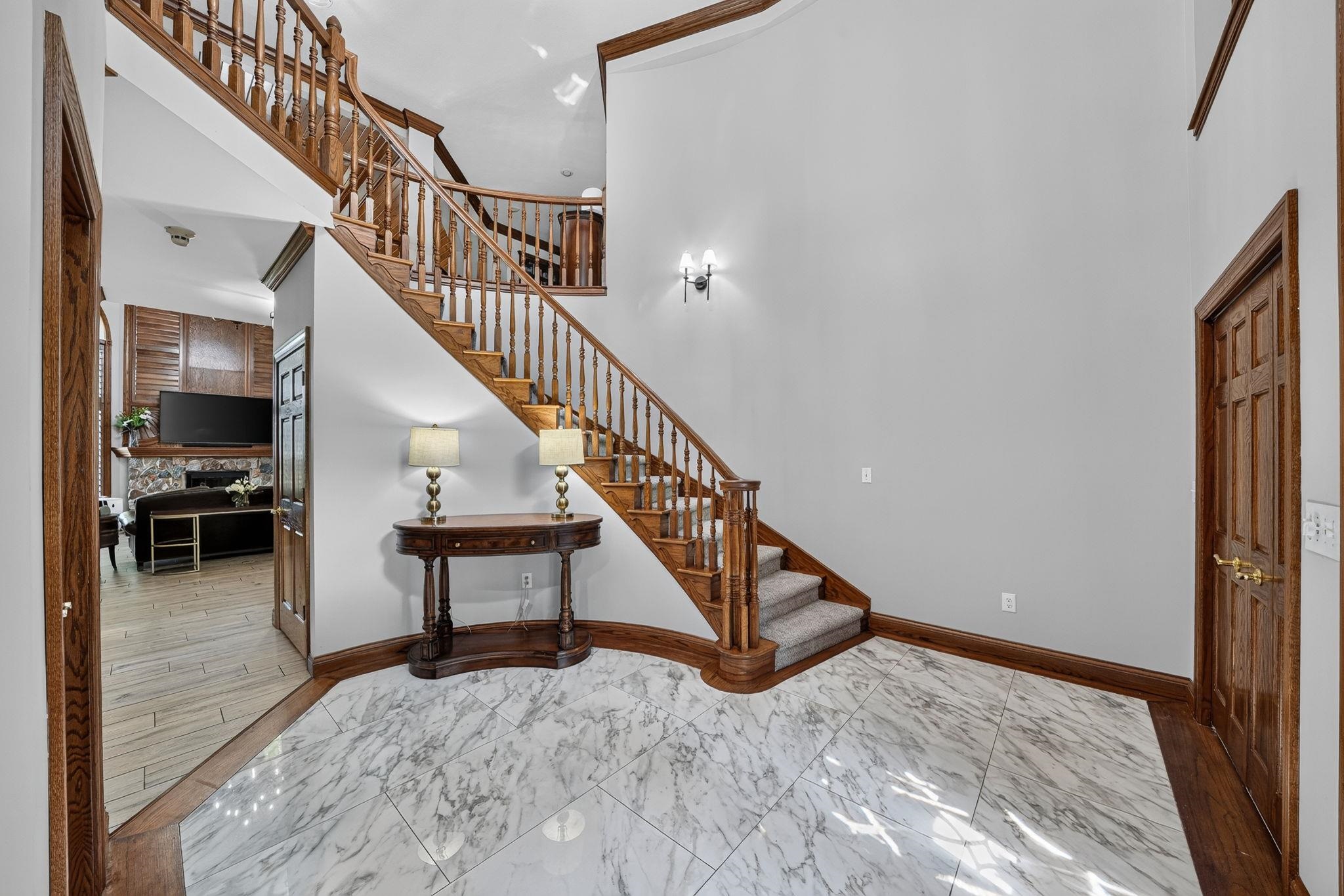 Two-story foyer featuring a grand staircase with wood balusters and handrail, white marble-look tile flooring, and dark wood trim