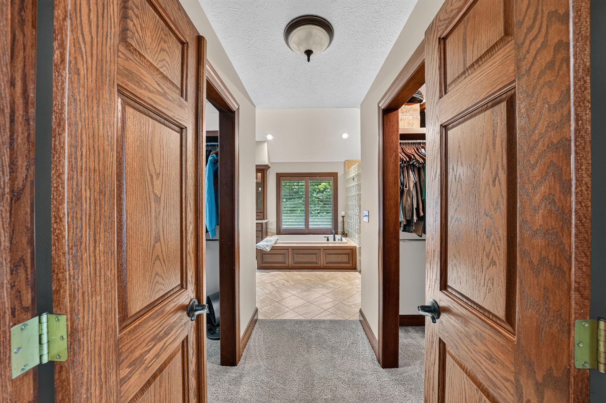 Herringbone tile flooring in the bathroom featuring a built-in soaking tub with shuttered window, flanked by two walk-in closets