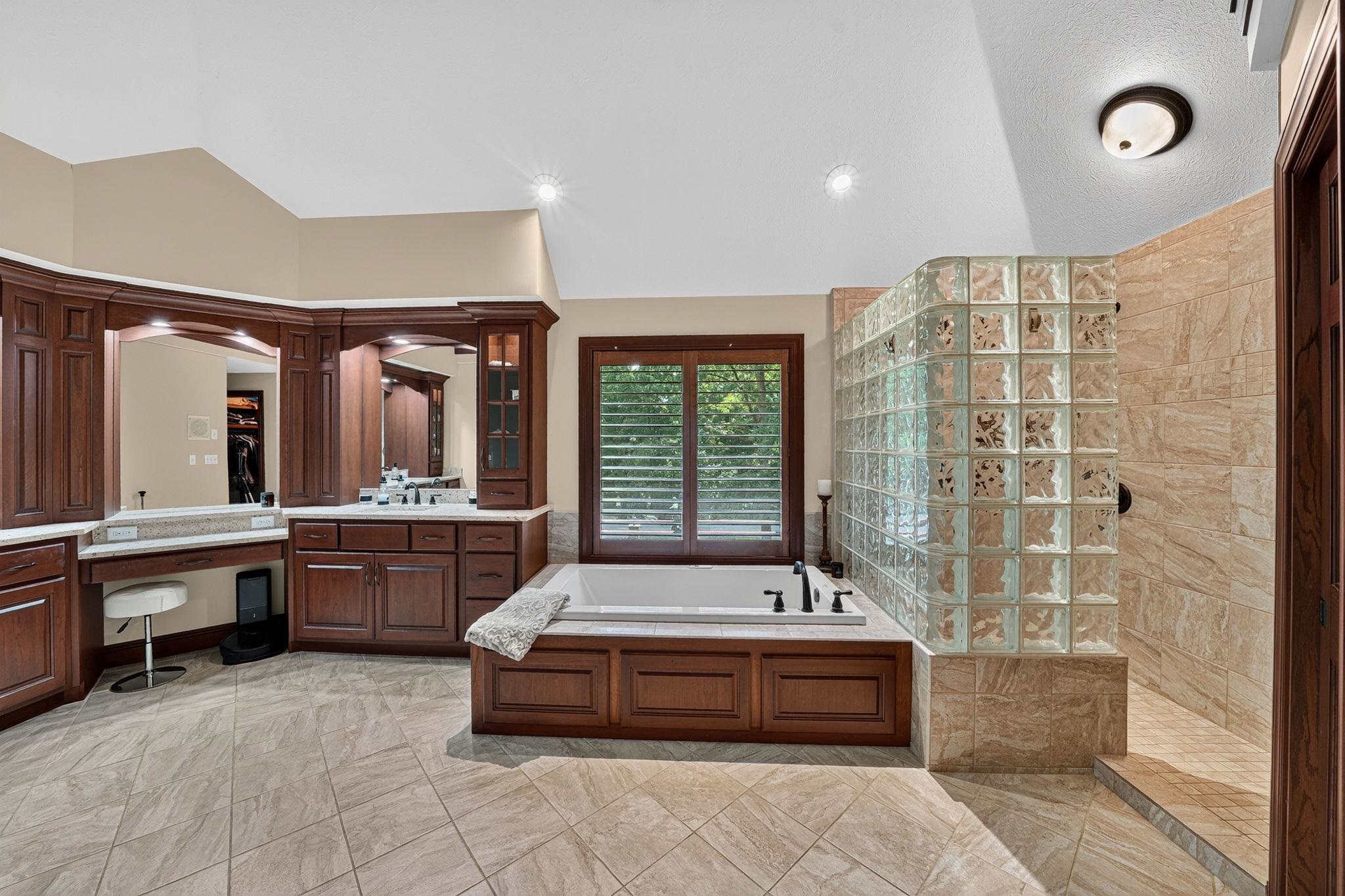 Bathroom featuring a built-in soaking tub, glass block shower enclosure, wood cabinetry, and tile flooring