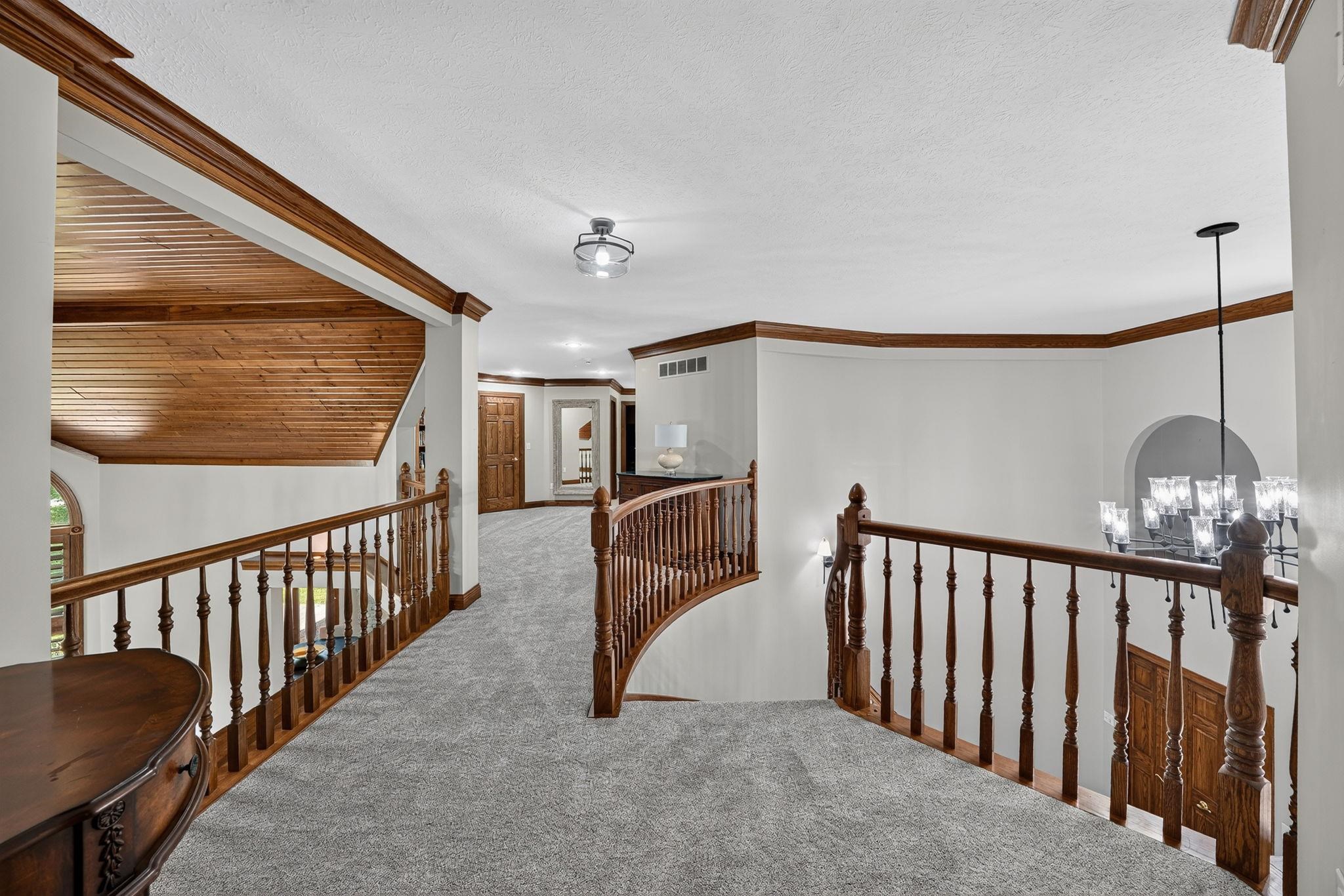 Expansive upper landing featuring plush carpeting, rich wood balusters, and crown molding accents