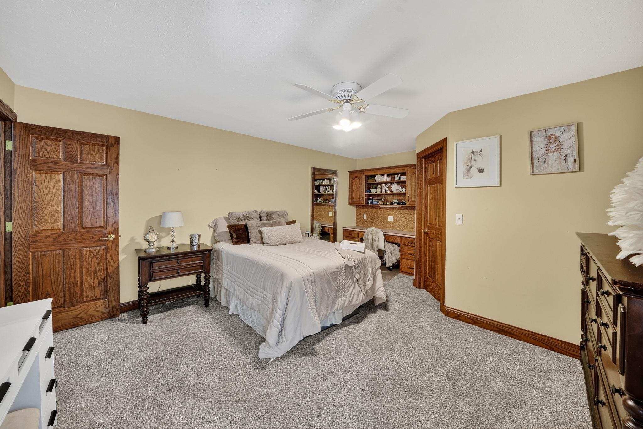 Carpeted room featuring a built-in desk with cabinetry, a ceiling fan, and hardwood doors and trim