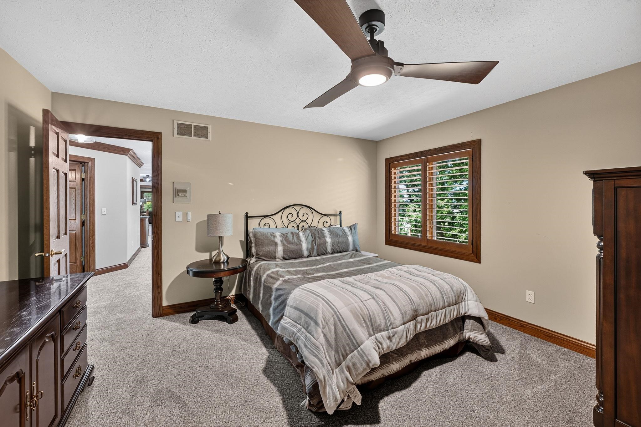 Carpeted room featuring a modern ceiling fan with integrated lighting, a window with interior wooden shutters, and dark wood trim throughout