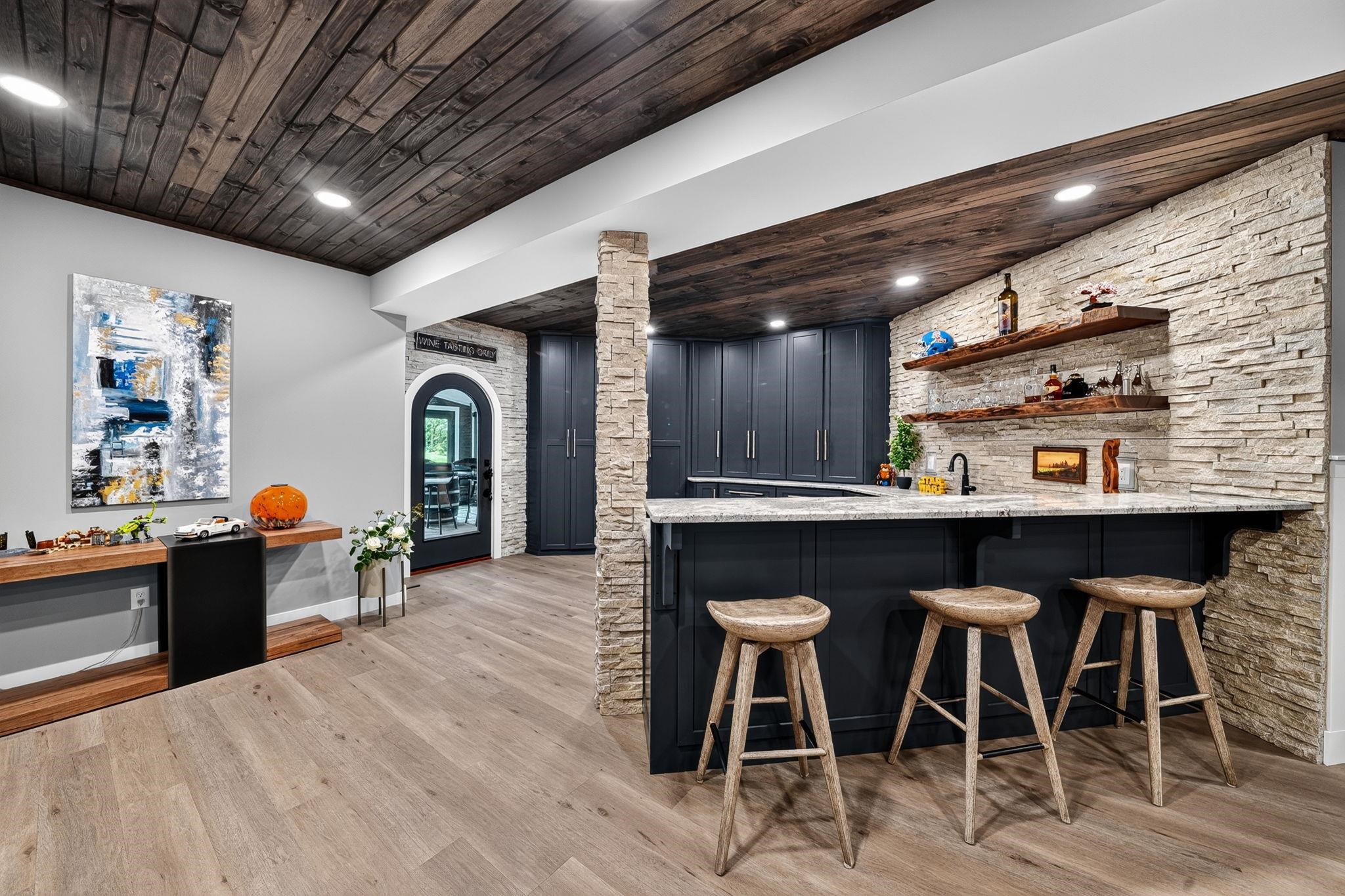 Lower-level entertainment space featuring a wet bar with dark cabinetry, light countertop, and stacked stone accent wall