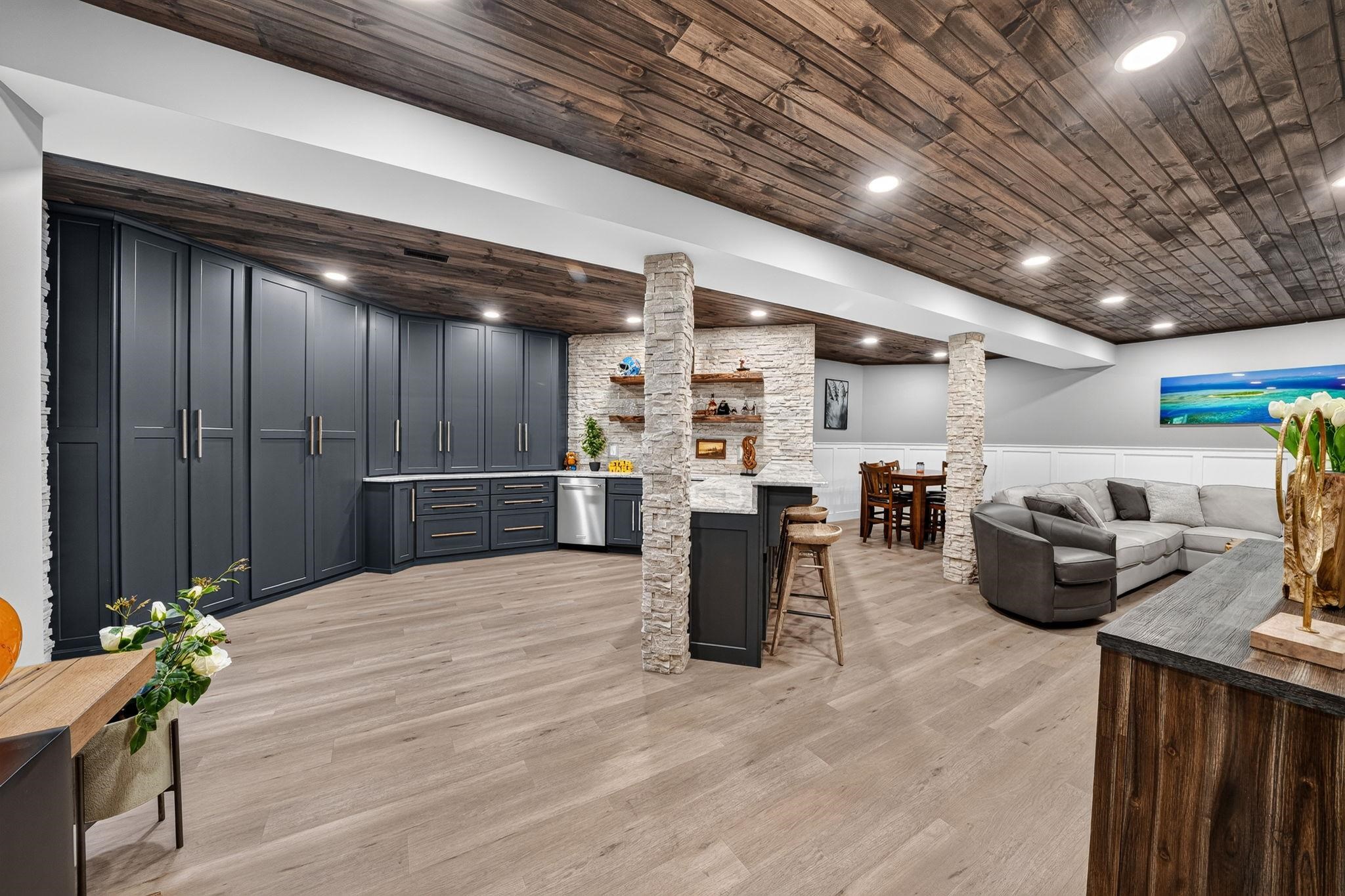 Expansive entertainment space featuring wood-finish flooring, a wood plank ceiling, stone-clad architectural columns, and recessed lighting