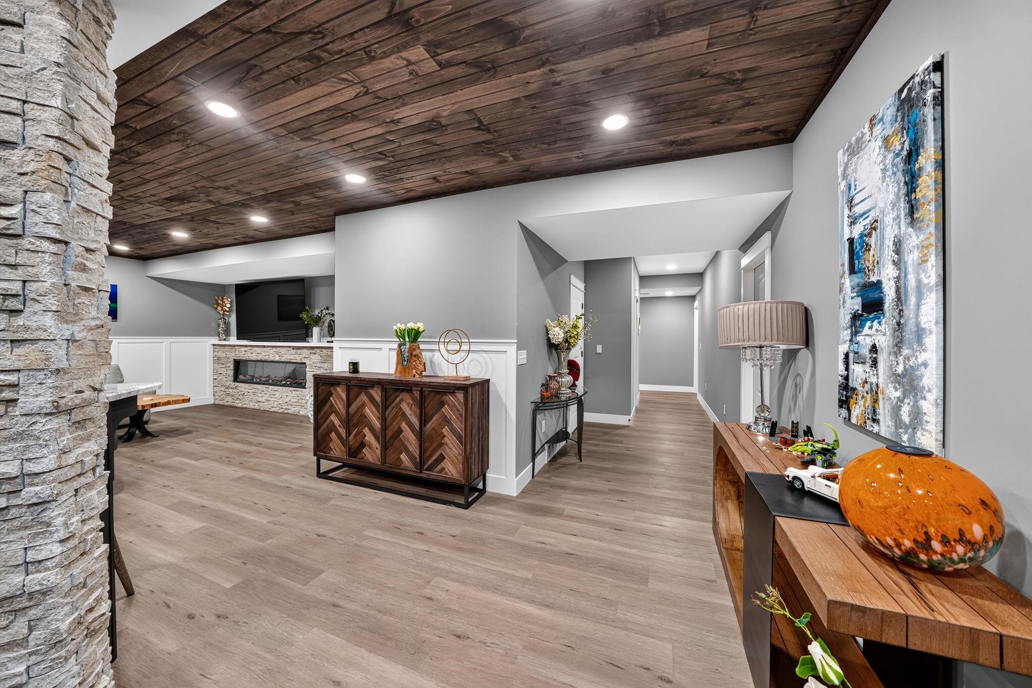 Finished lower level with wood-finish flooring, stone accent column, and a wood plank ceiling featuring recessed lighting