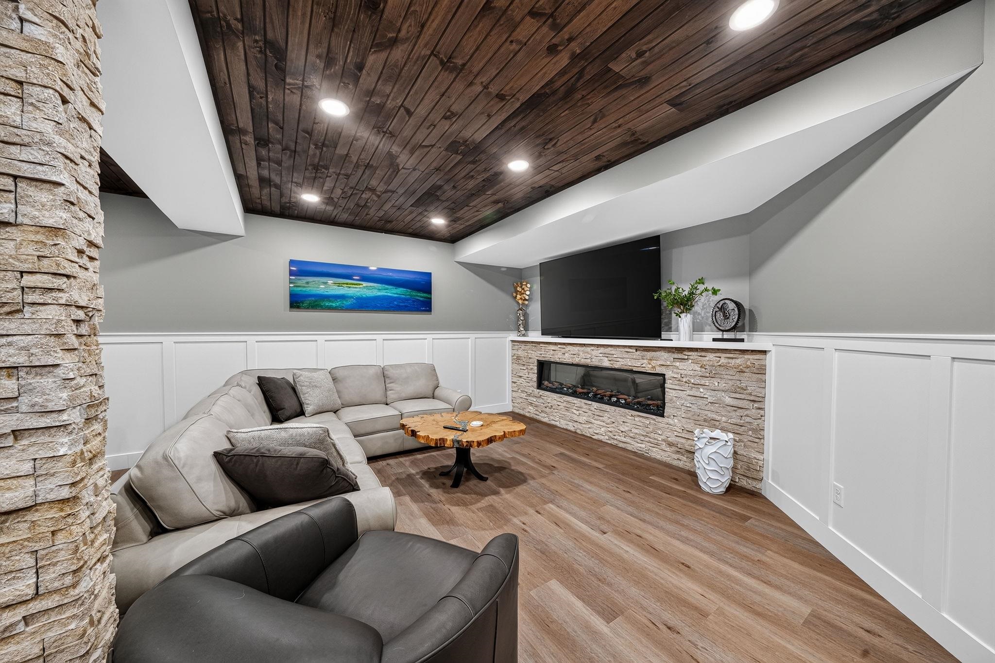 Recreational room featuring a wood-finish plank ceiling with recessed lighting, a built-in electric fireplace with stone surround, a white quartz hearth, and wood-finish flooring