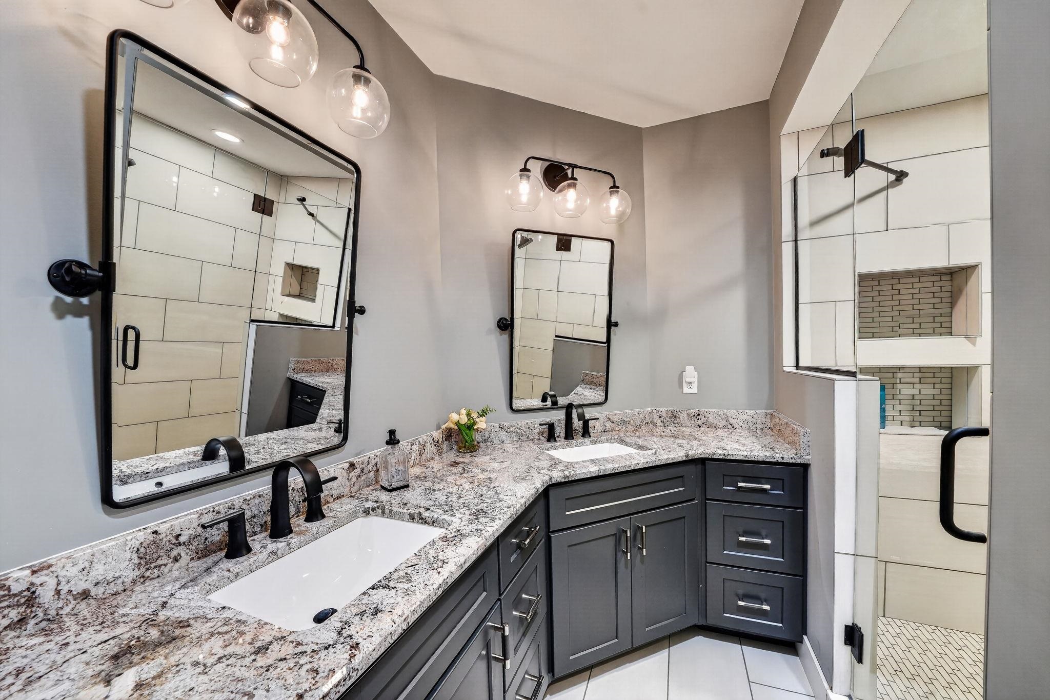 Vanity area featuring a dual sink arrangement with integrated basins, a granite countertop, dark gray cabinetry, and matte black fixtures