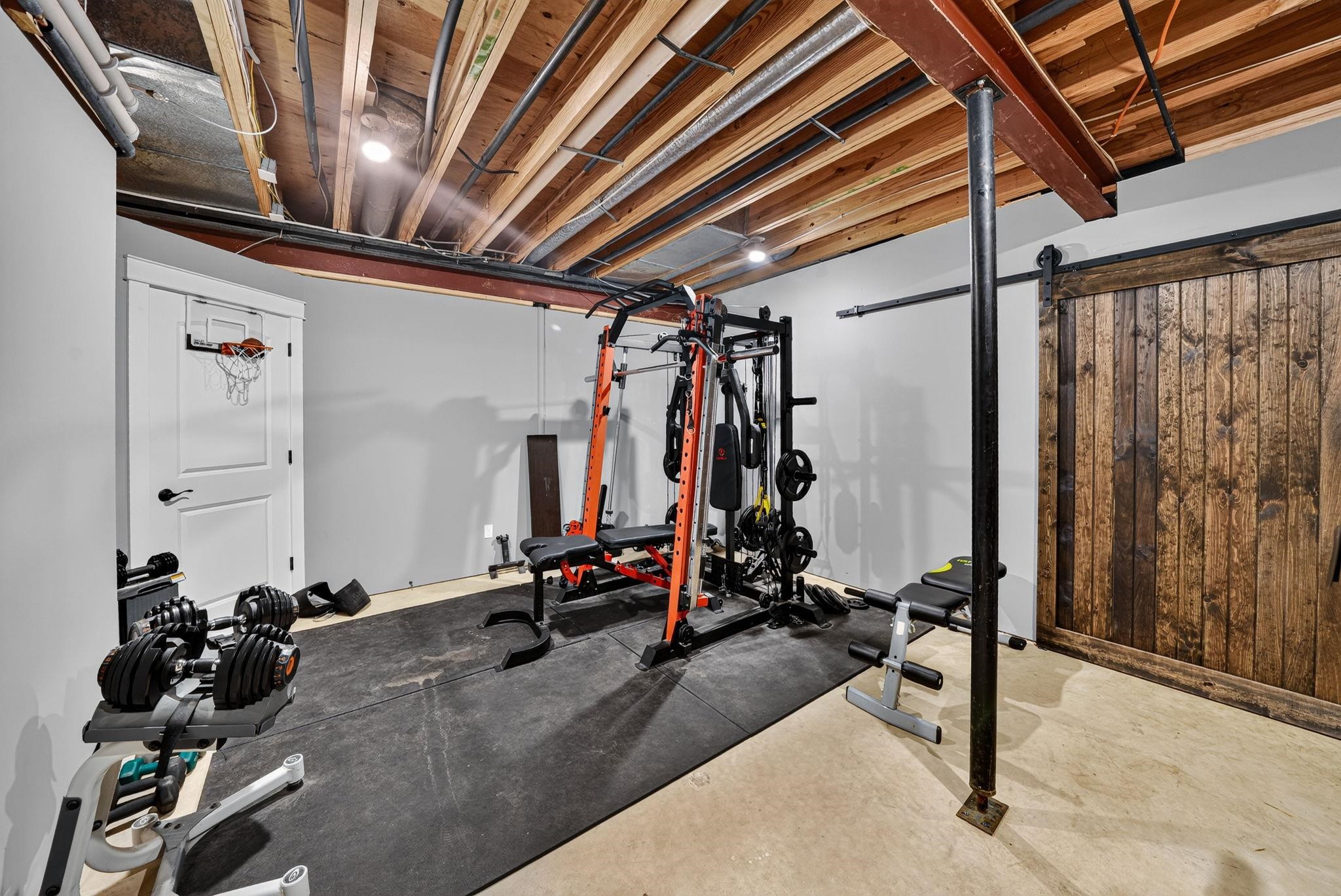 Unfinished basement area featuring exposed ceiling joists, overhead lighting, a barn door, and a permanent structural support column