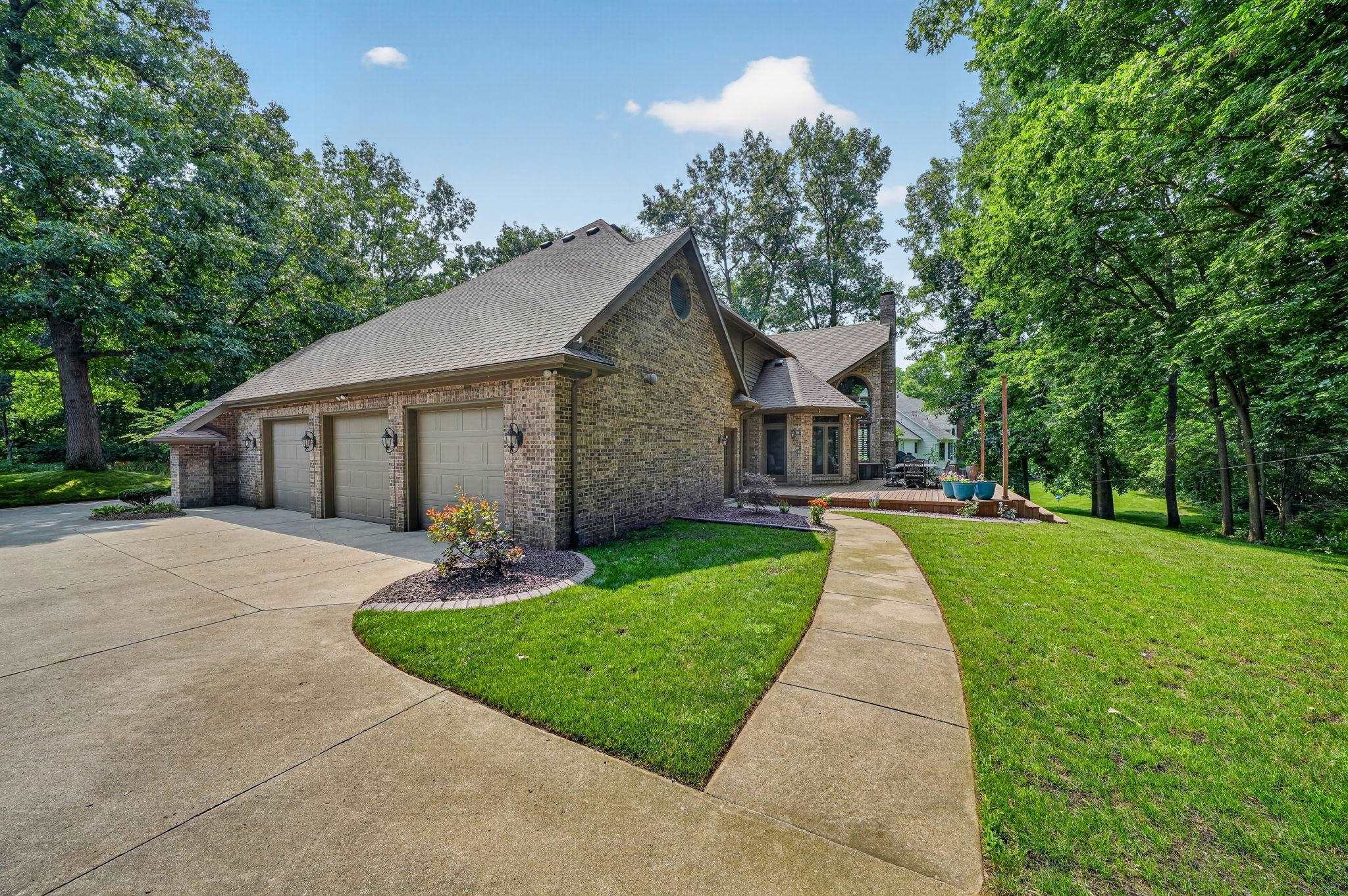 Stone veneer and brick exterior with a three-car garage, concrete driveway, and a flagstone patio