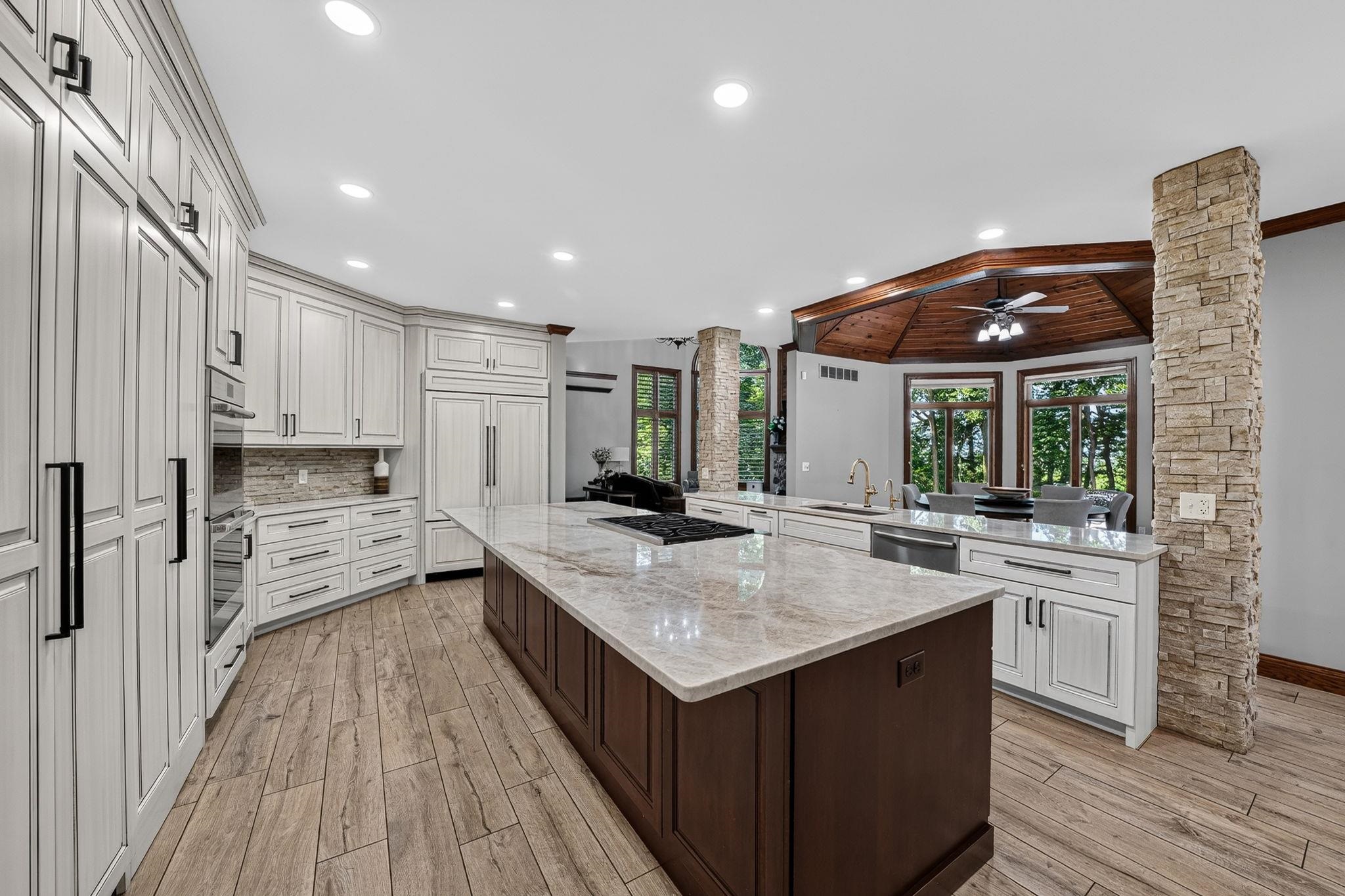 Gourmet kitchen with a large center island, integrated appliances, wood-finish flooring, a decorative stone column, and a tray ceiling with a wood plank finish