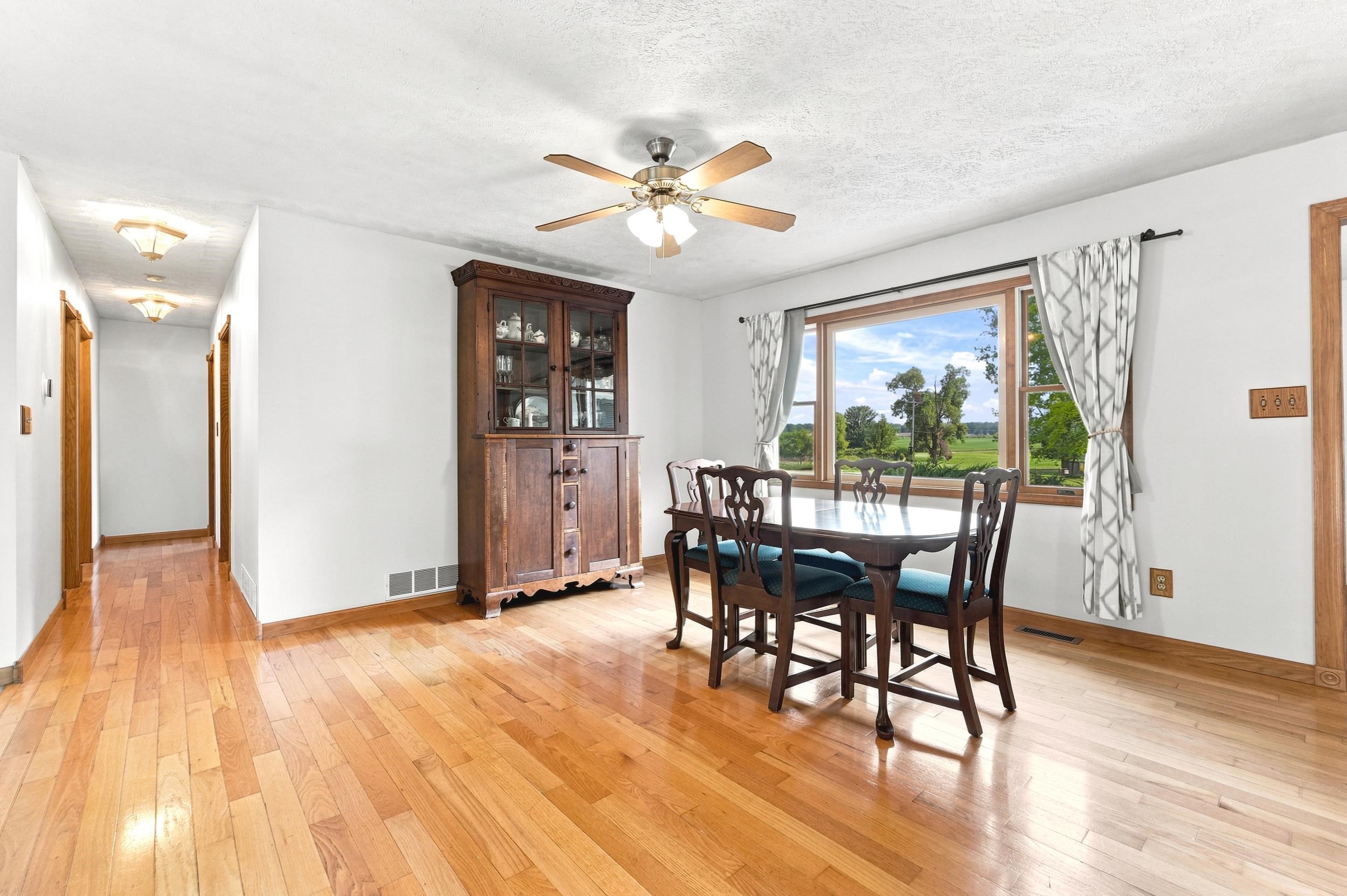 Dining area featuring wood-finish flooring, a ceiling fan with integrated lighting, and a large window overlooking a verdant landscape